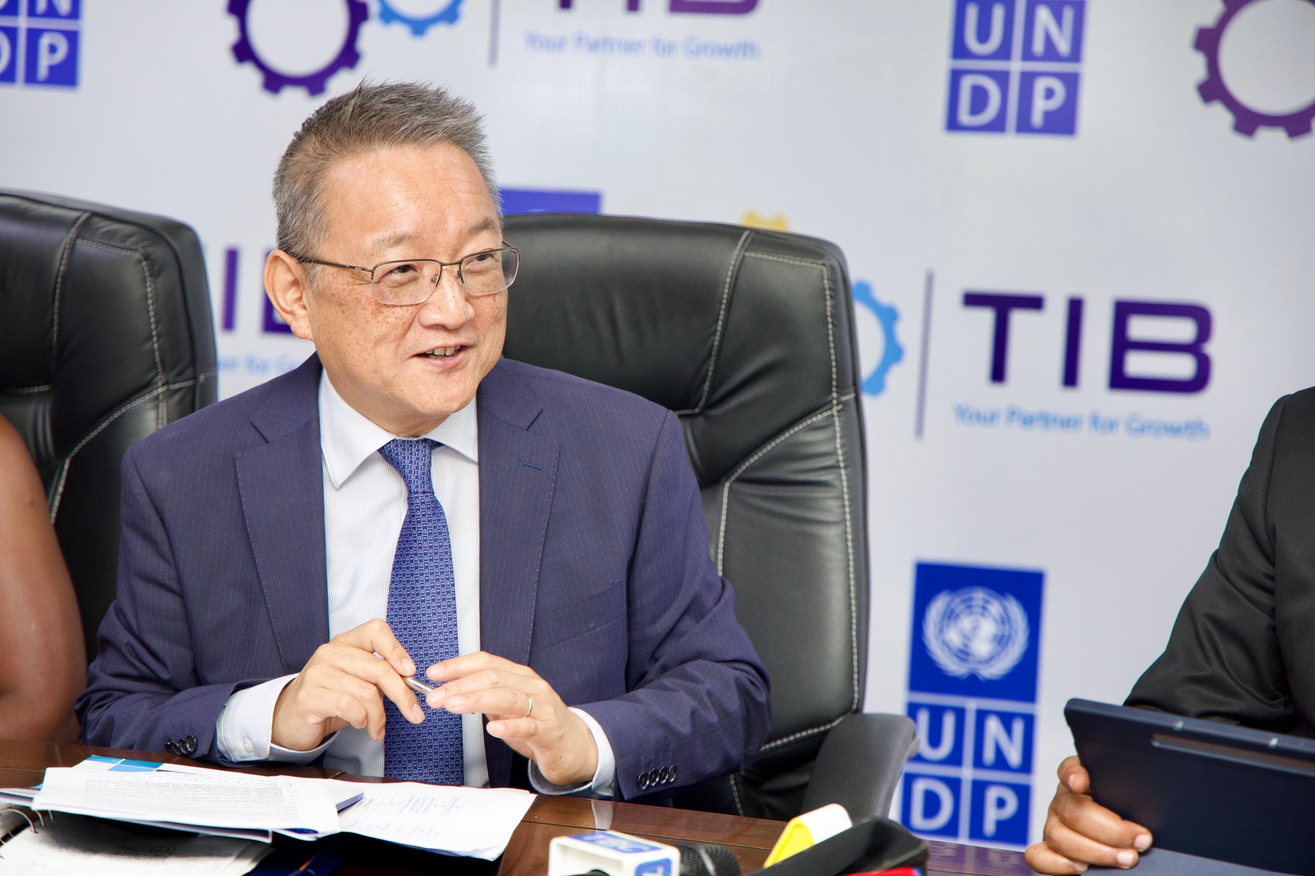 Blurry man in a suit signs papers at a table with UNDP banners in the background.