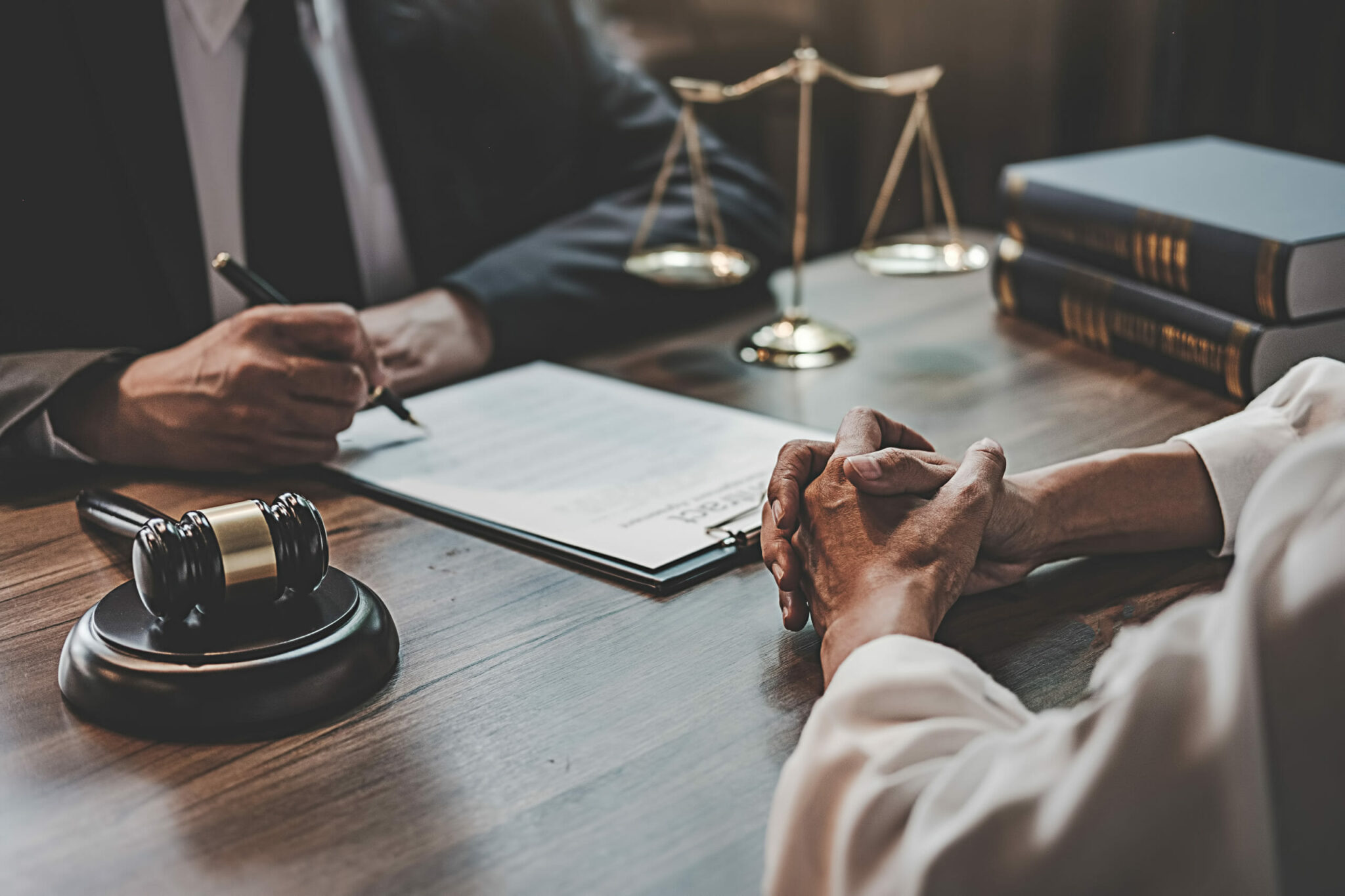 Two people sign documents at a lawyer's desk, with a gavel and scales behind.