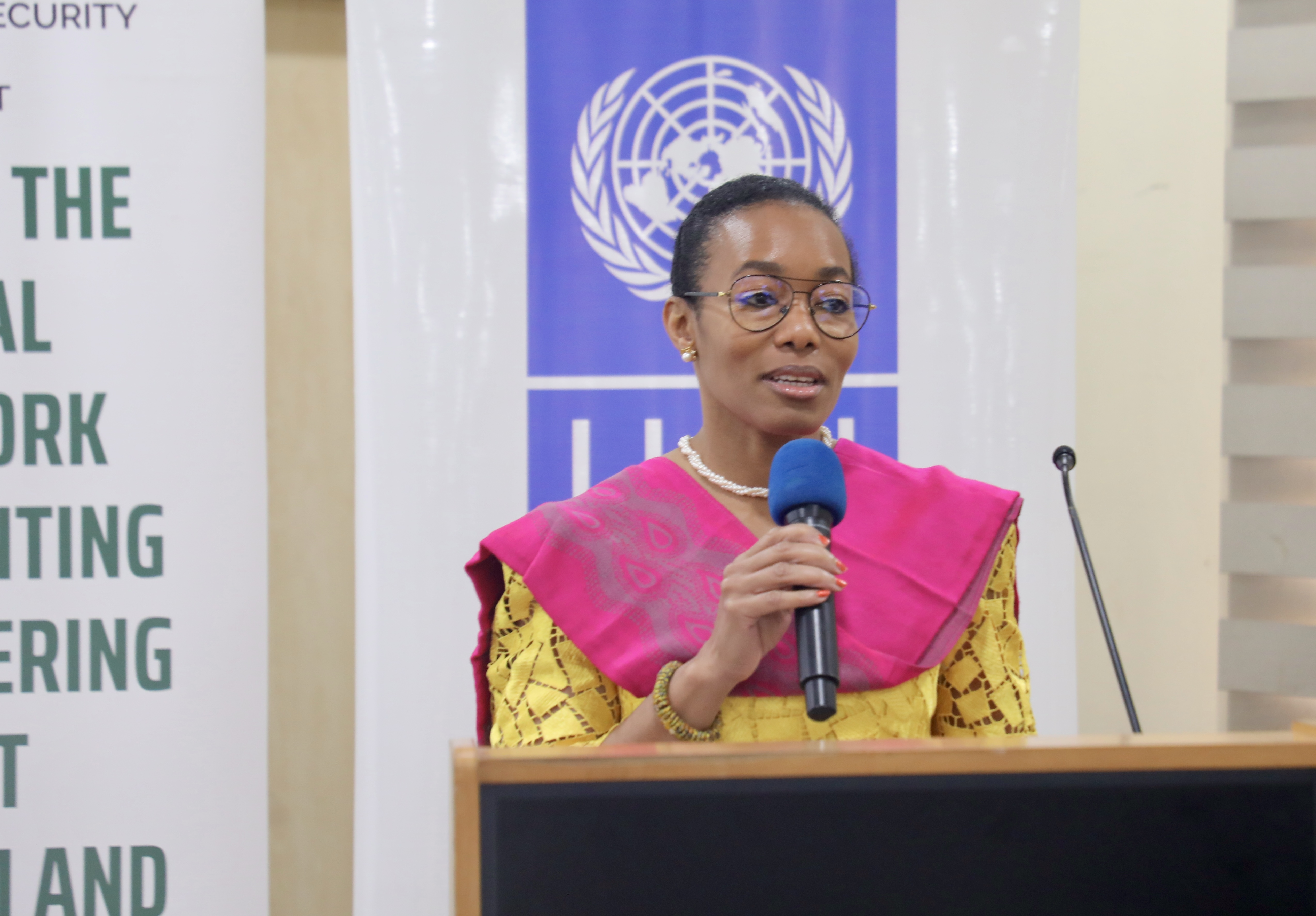 Photograph: speaker at podium with UN banner in background, wearing a pink top with gold sleeves.