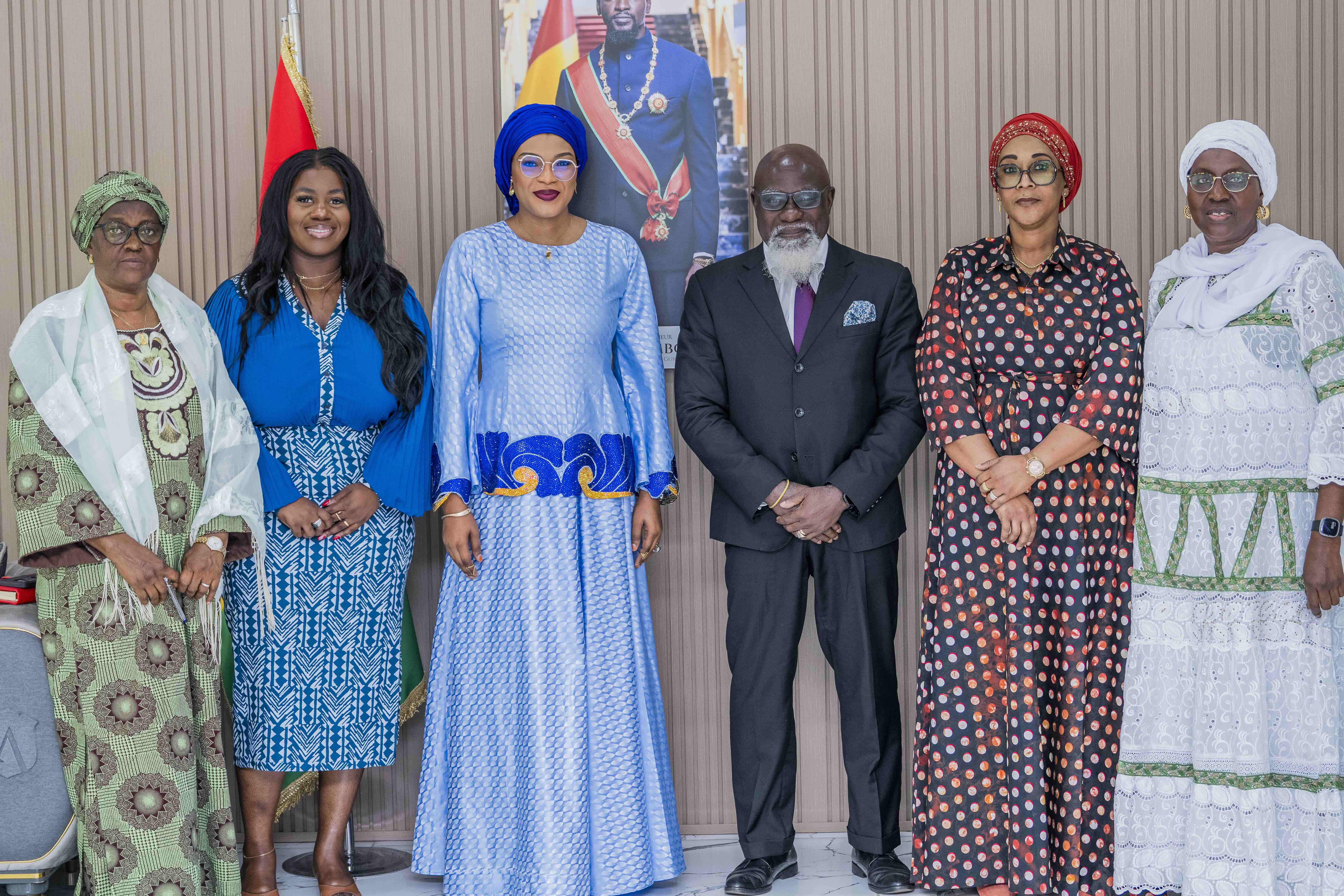 Photo: Six people in colorful outfits posing in front of a flag.