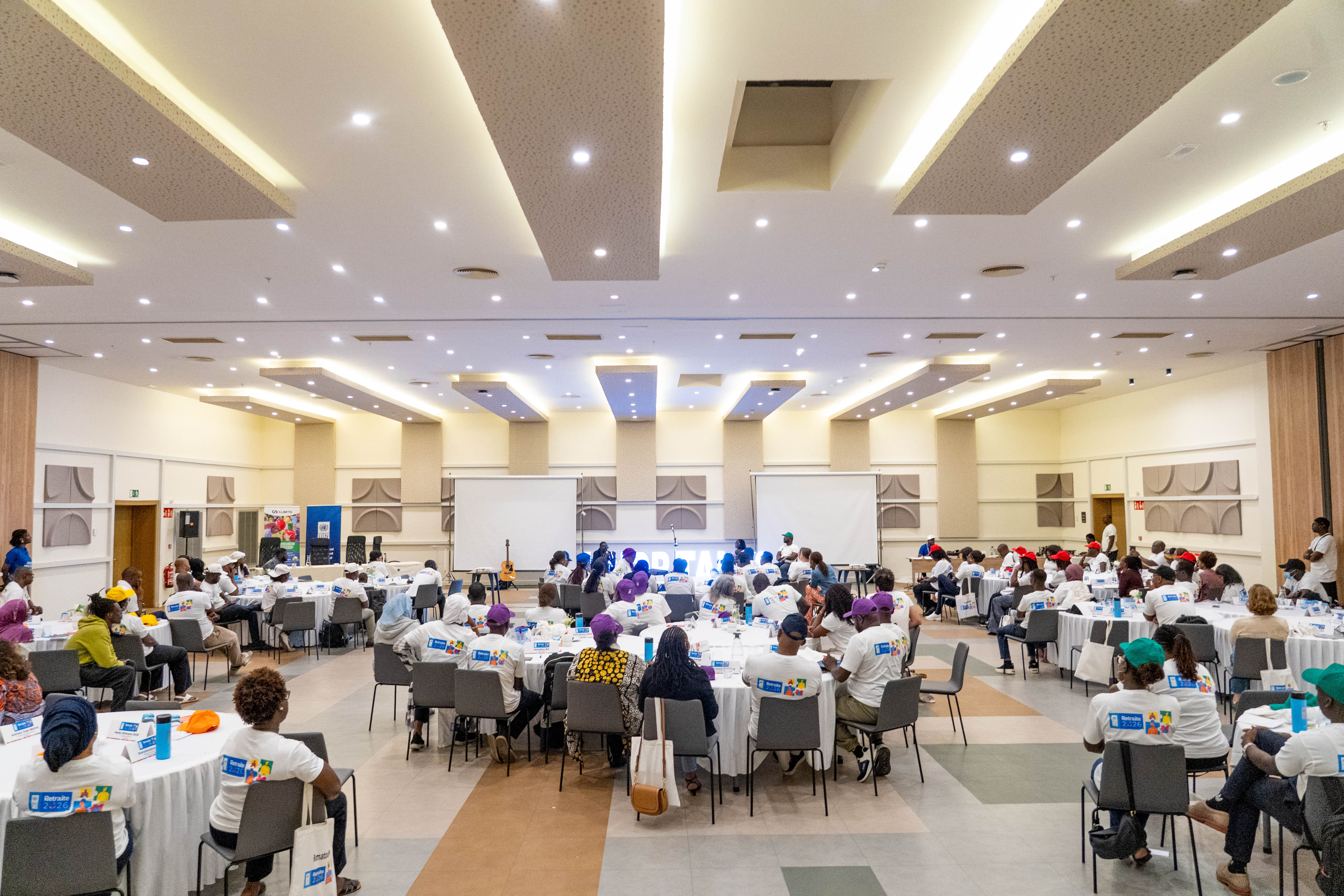 Photograph of a large conference hall with attendees seated at tables facing a stage.