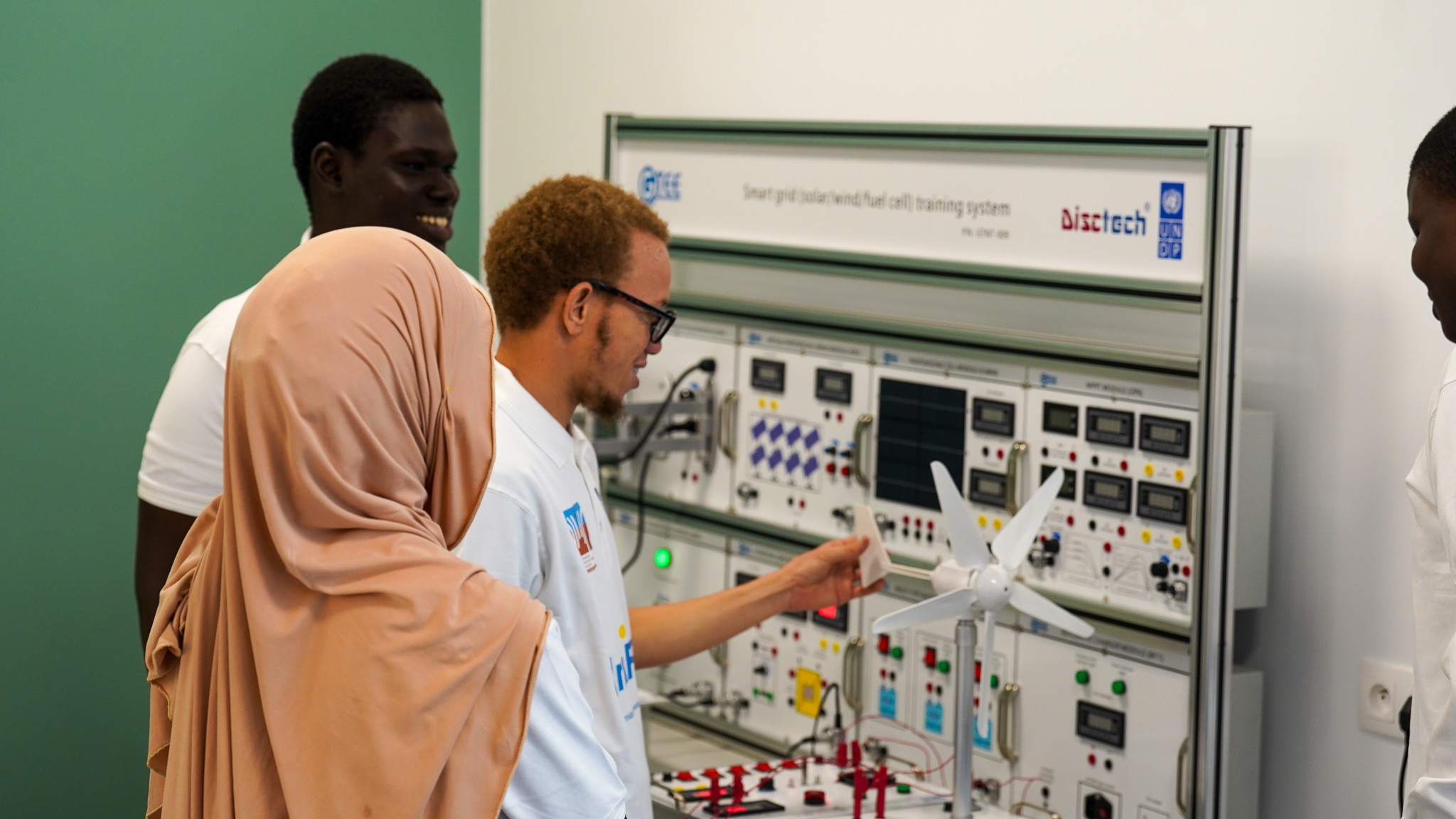 Un groupe d'étudiants examine un grand tableau électrique équipé d'interrupteurs et de compteurs.