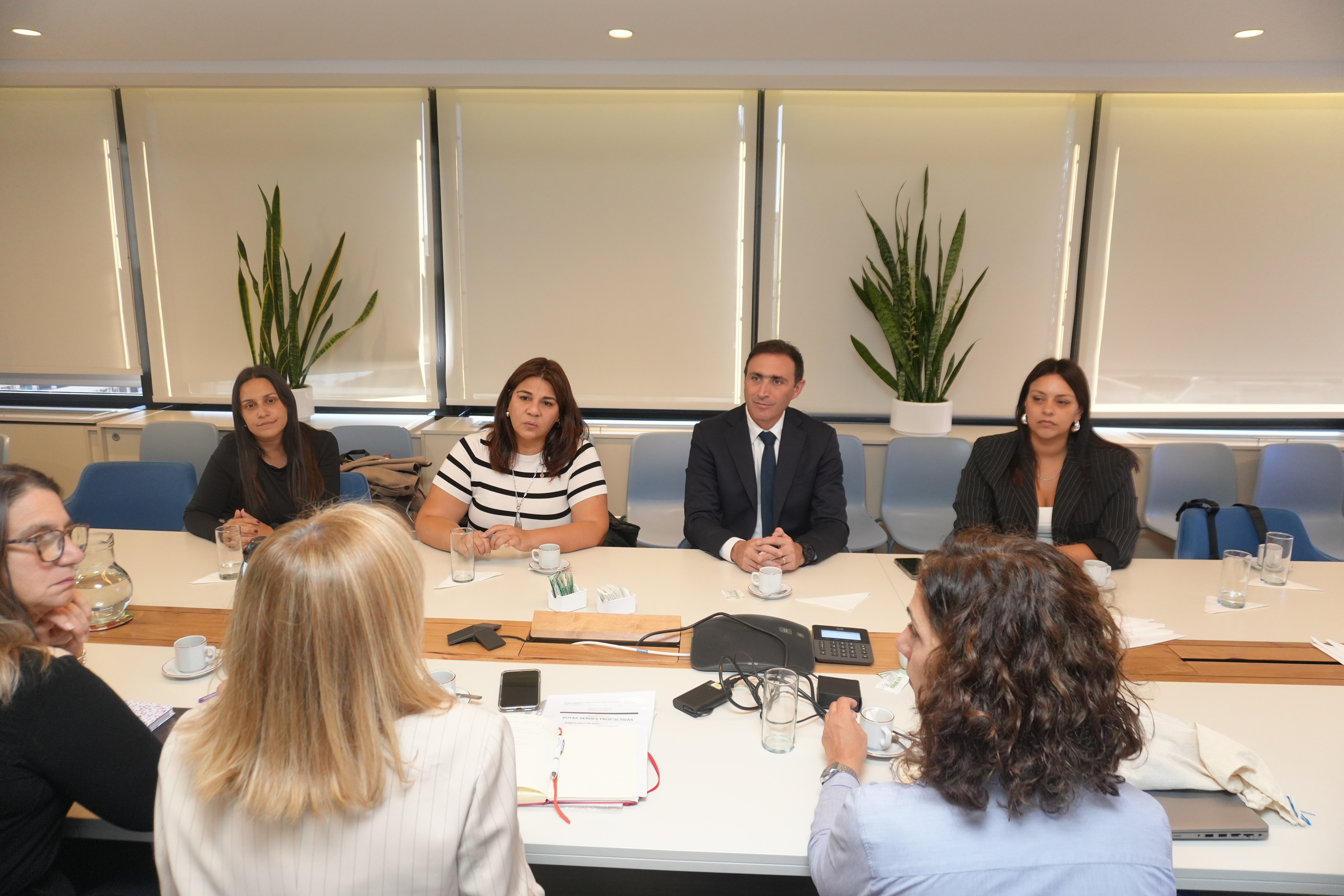 Group of professionals around a conference table in a bright meeting room, discussing documents.