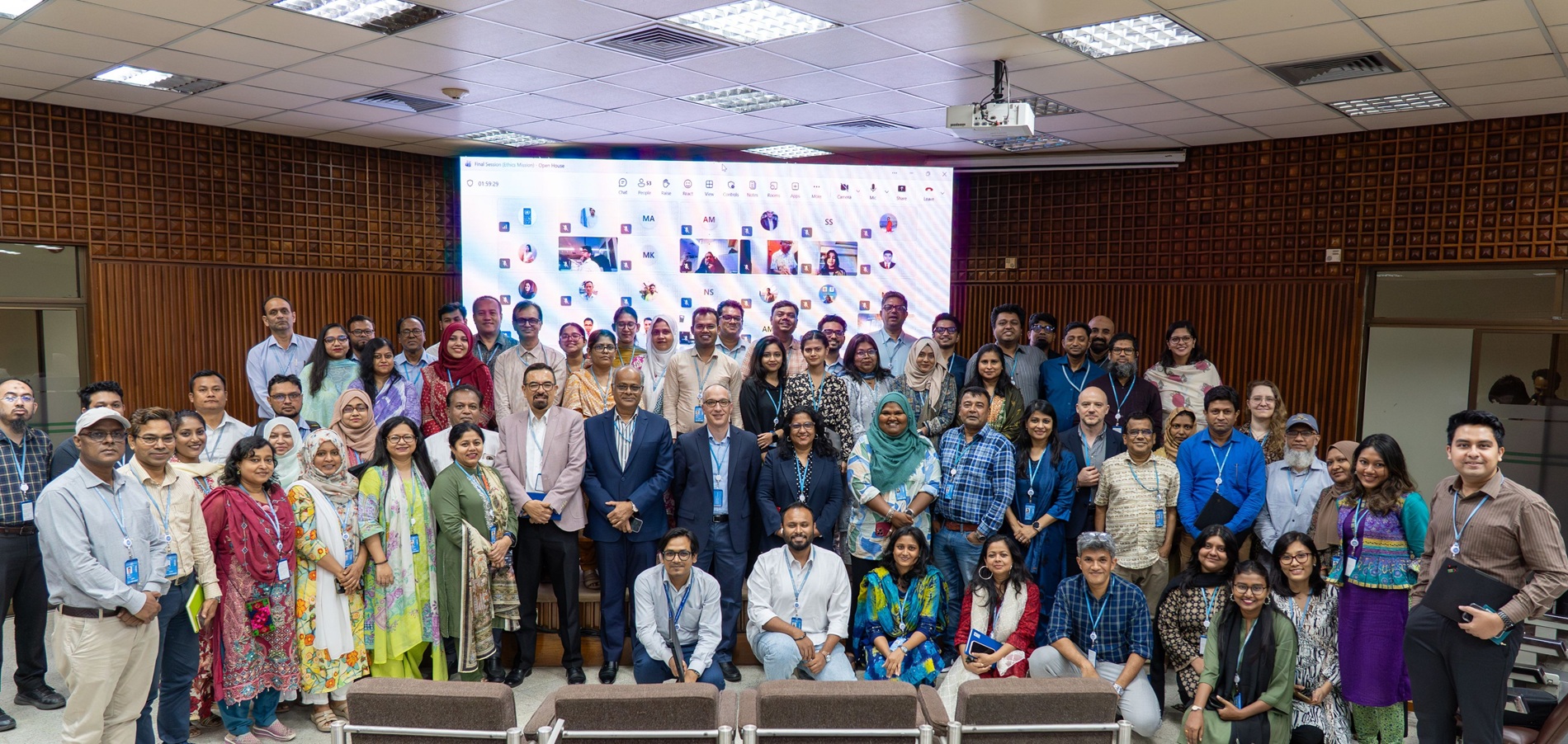Group photo of diverse people in a conference room, posing in front of a banner.