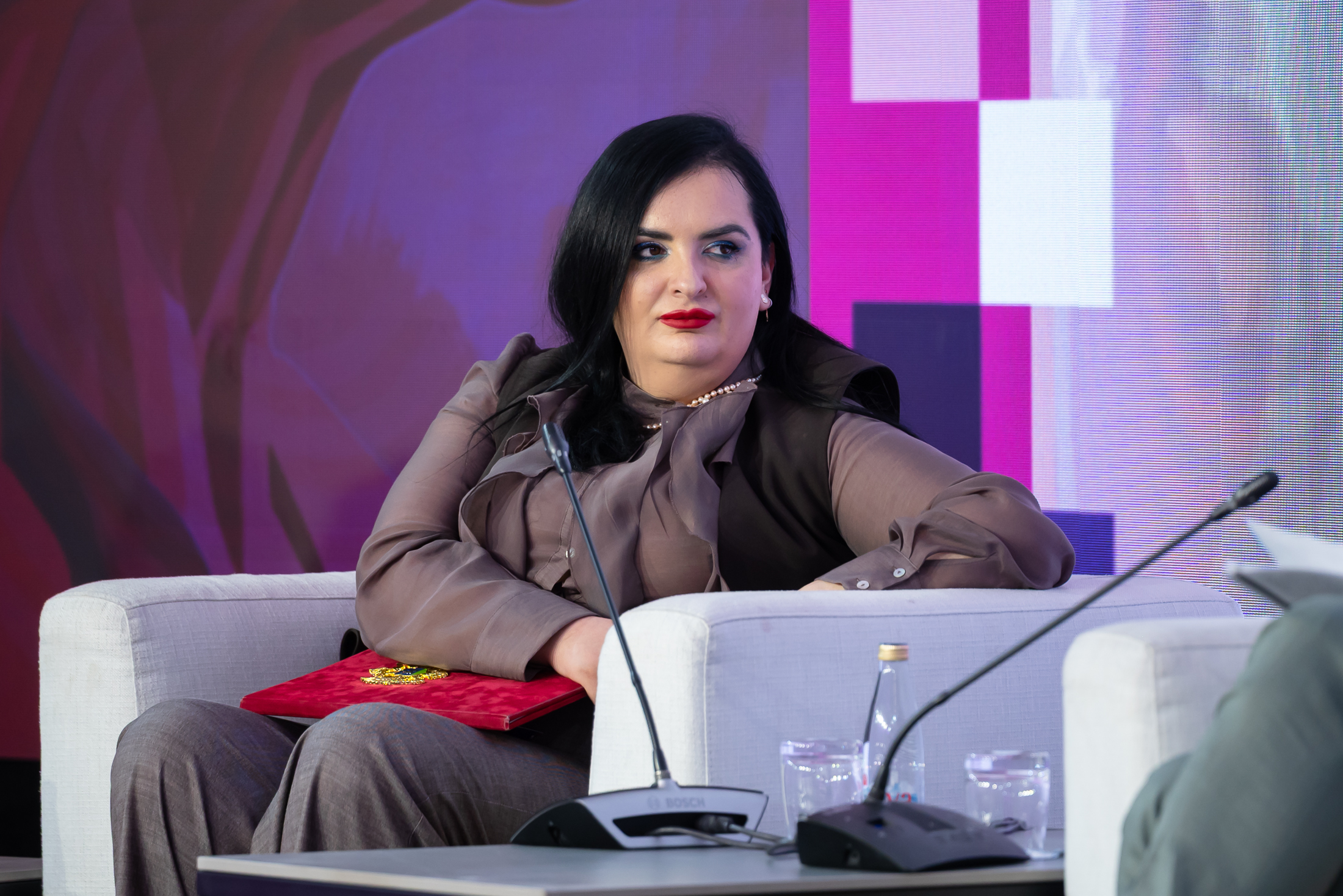 Speaker on a gray couch, microphone on a stand, purple backdrop.