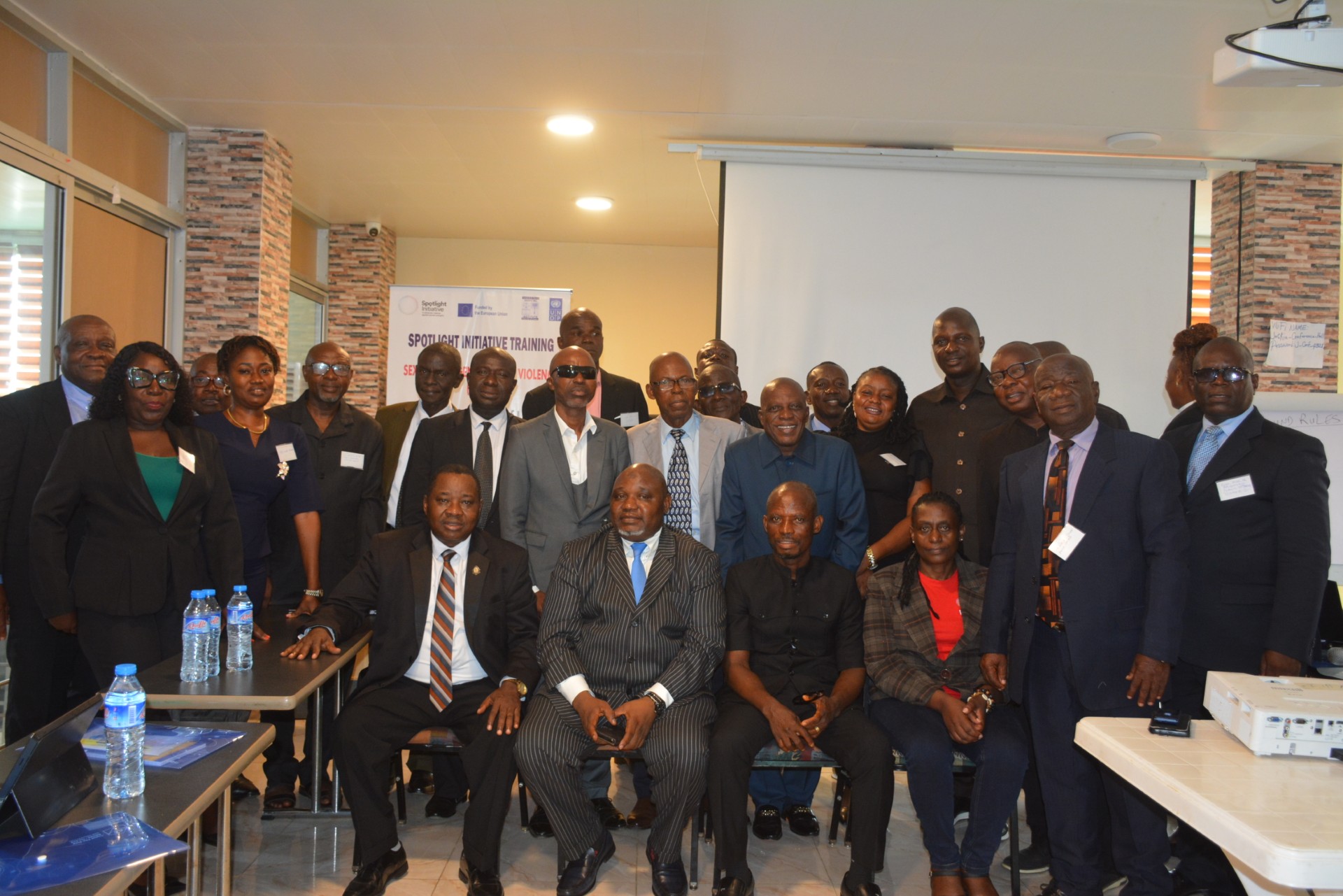 Group photo of diverse professionals in a conference room, with banners and a projection screen.