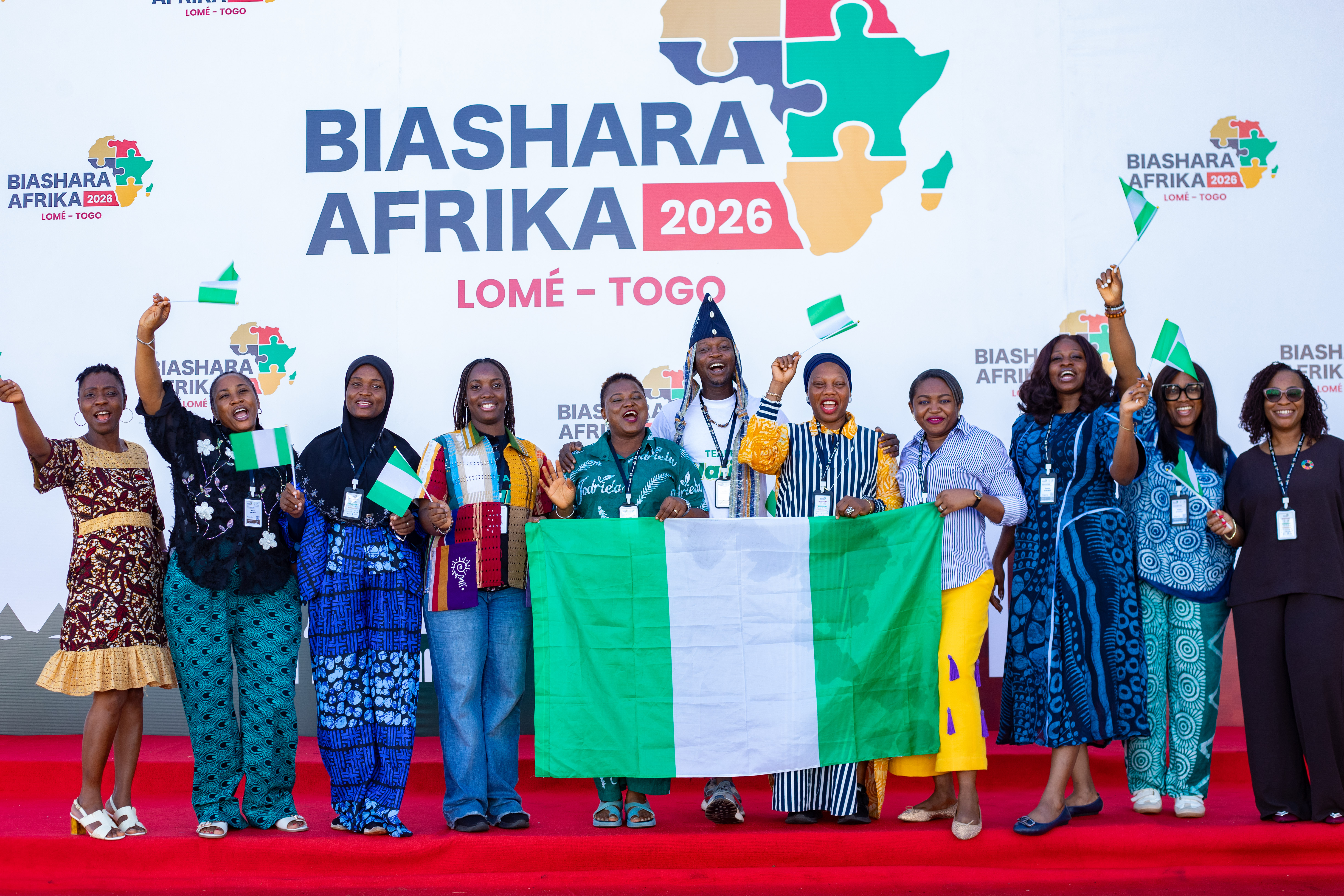 Diverse group on a red stage holding a Nigerian flag at Biashara Afrika 2020, Lomé, Togo.