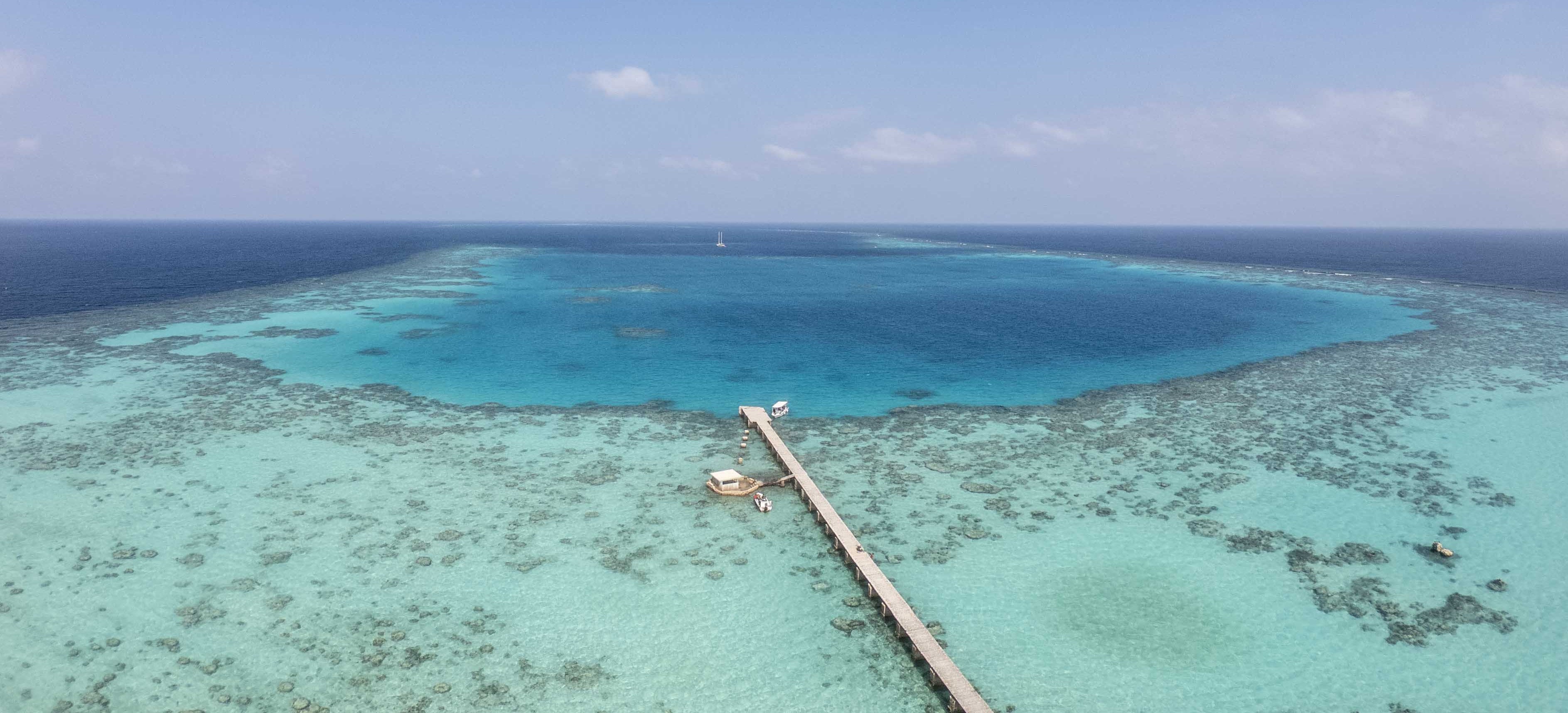 Aerial view of a turquoise lagoon with a wooden pier extending into the sea.