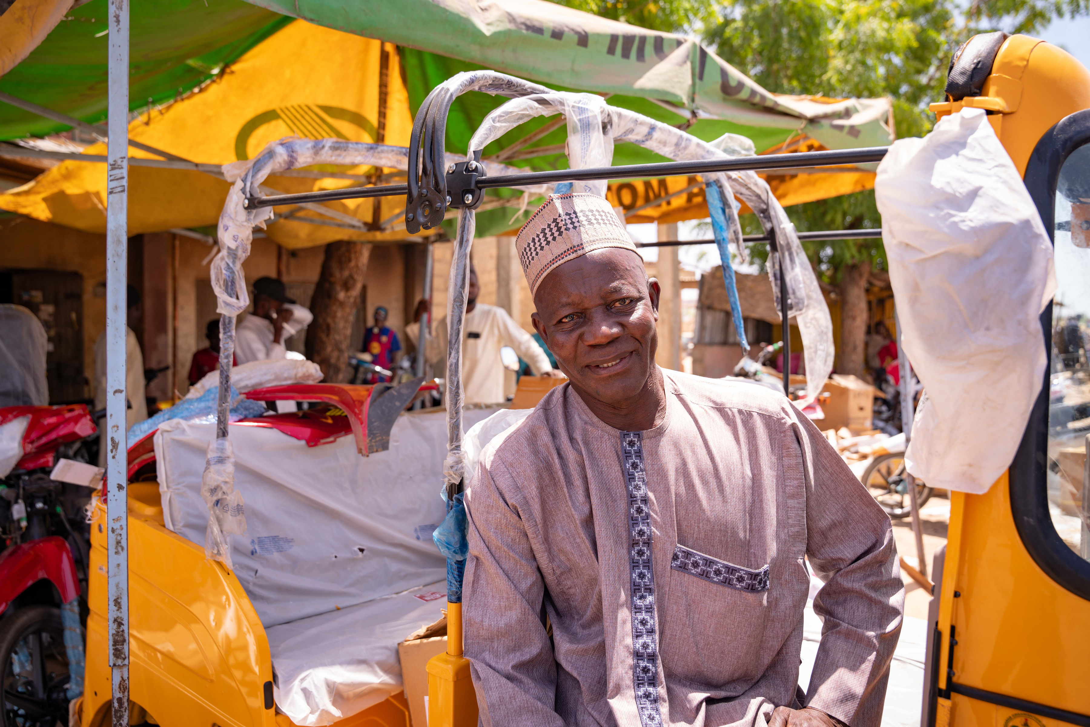Person with blurred face wearing a traditional kurta in a cycle rickshaw under a yellow canopy.
