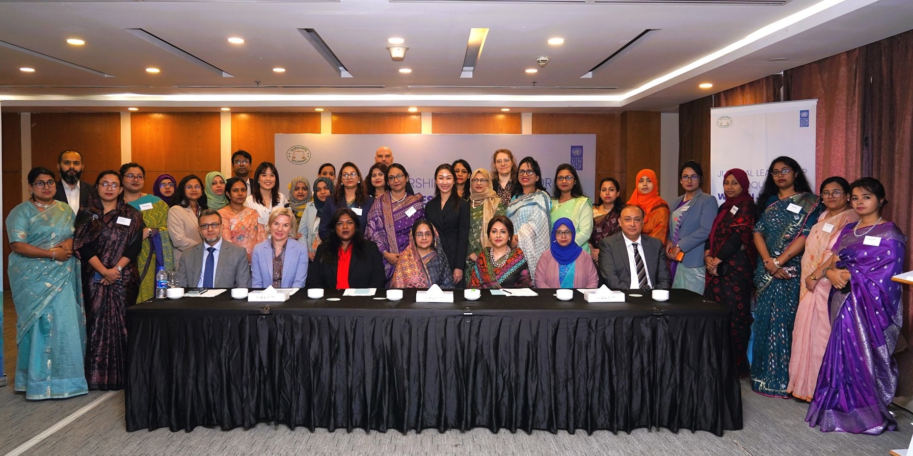 Group photograph of professionals in colorful attire standing behind a long table at a conference.