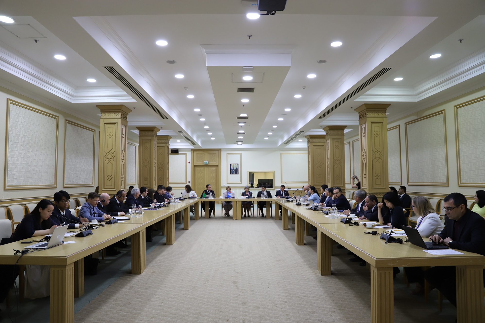 Photograph of a formal meeting in a large conference room with attendees around long tables.