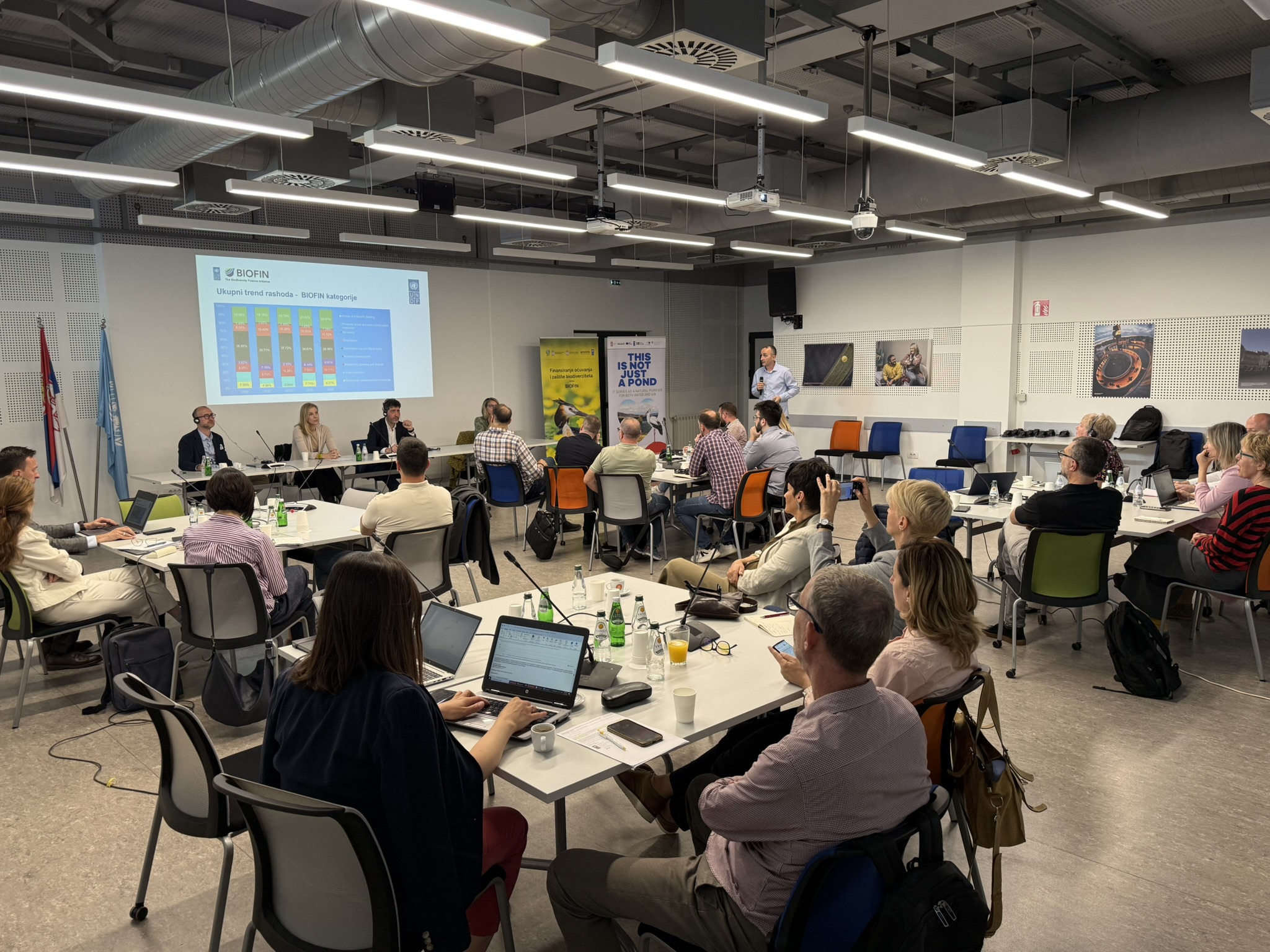Participants at tables with laptops in a workshop; projector screen shows charts.