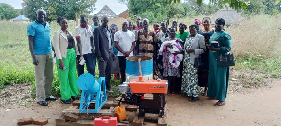 Group of people around a small red tractor on a dirt road with tents in the background.