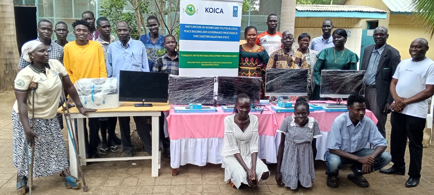 Photograph: Group of people outdoors behind a long table with a banner and a laptop.