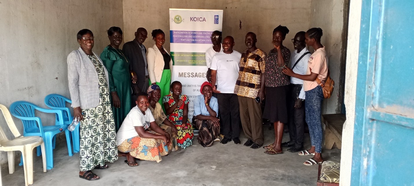 Group of people posing for a photo in a small room with a banner behind them.