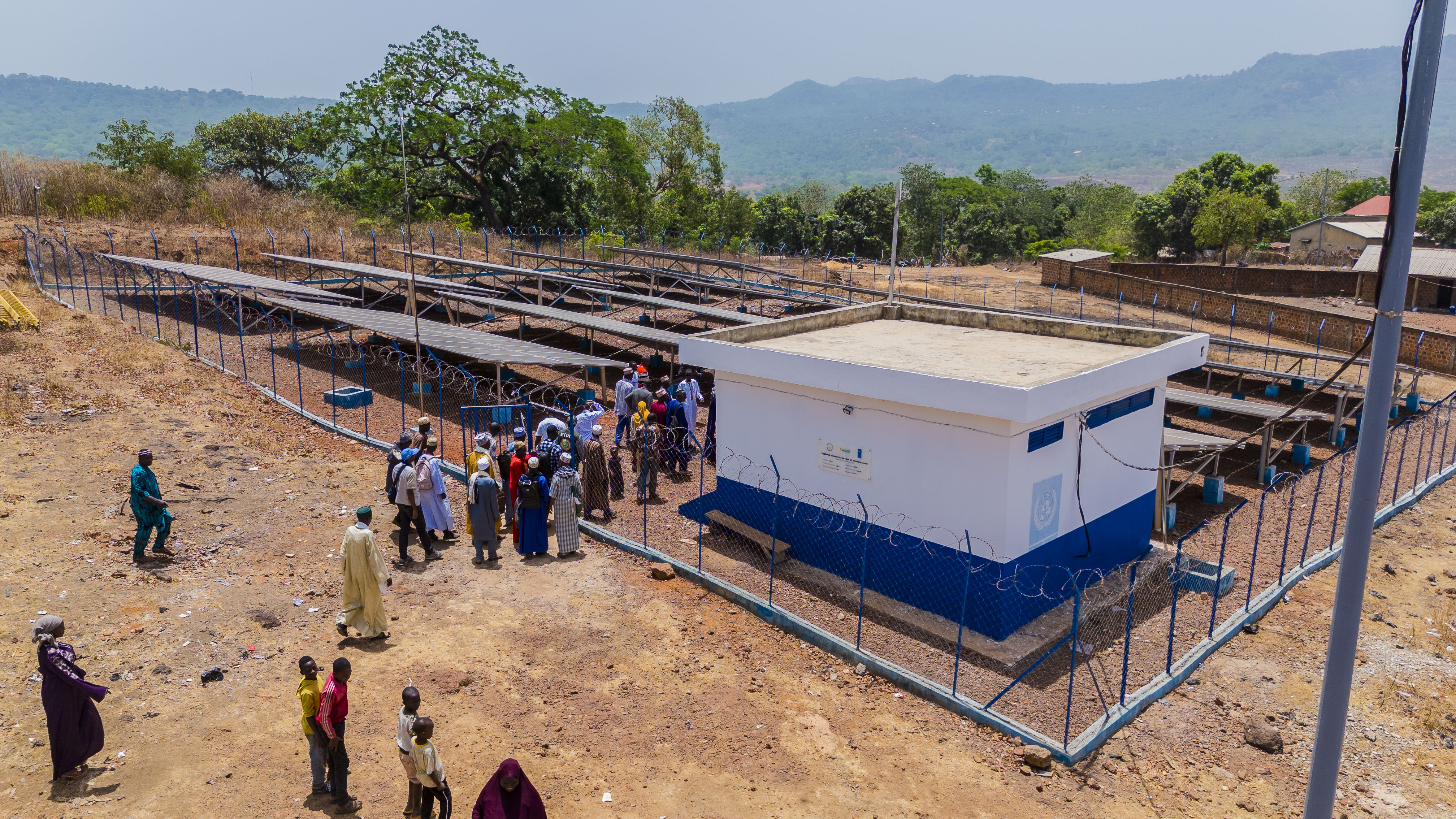People gather near a blue-and-white portable building on a dusty construction site.