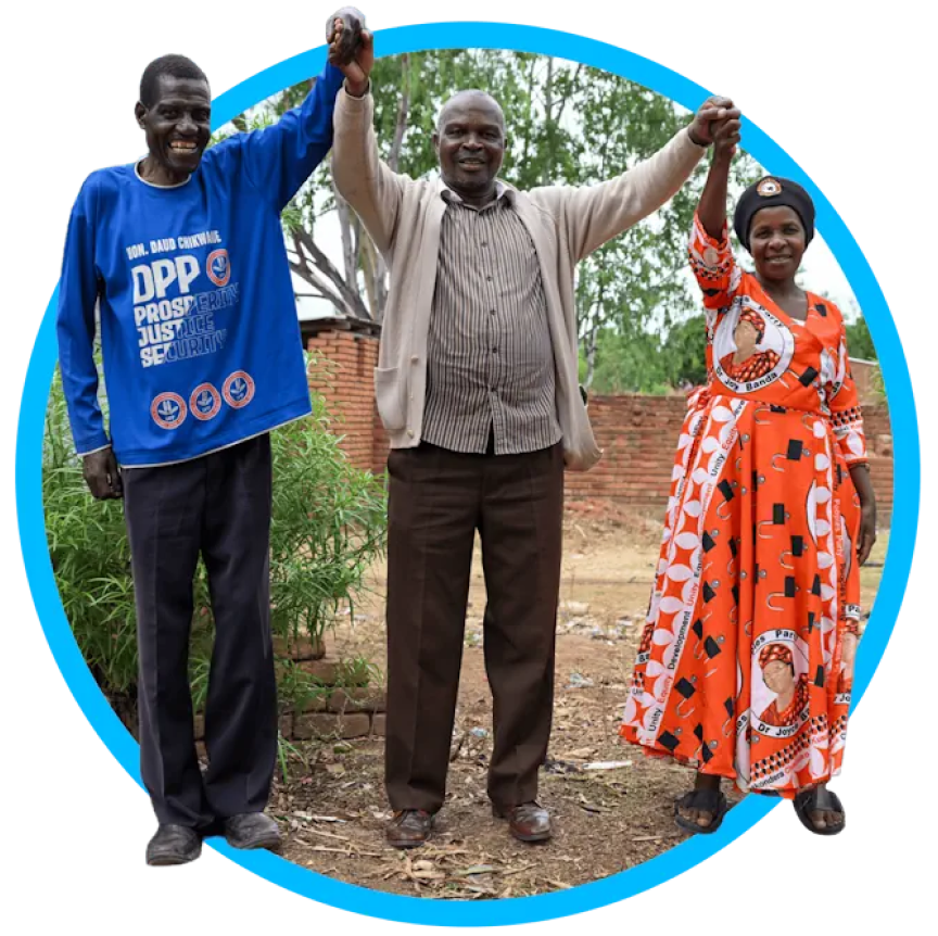 Photo of three people outdoors, raising hands; left in blue, middle in tan, right in orange.