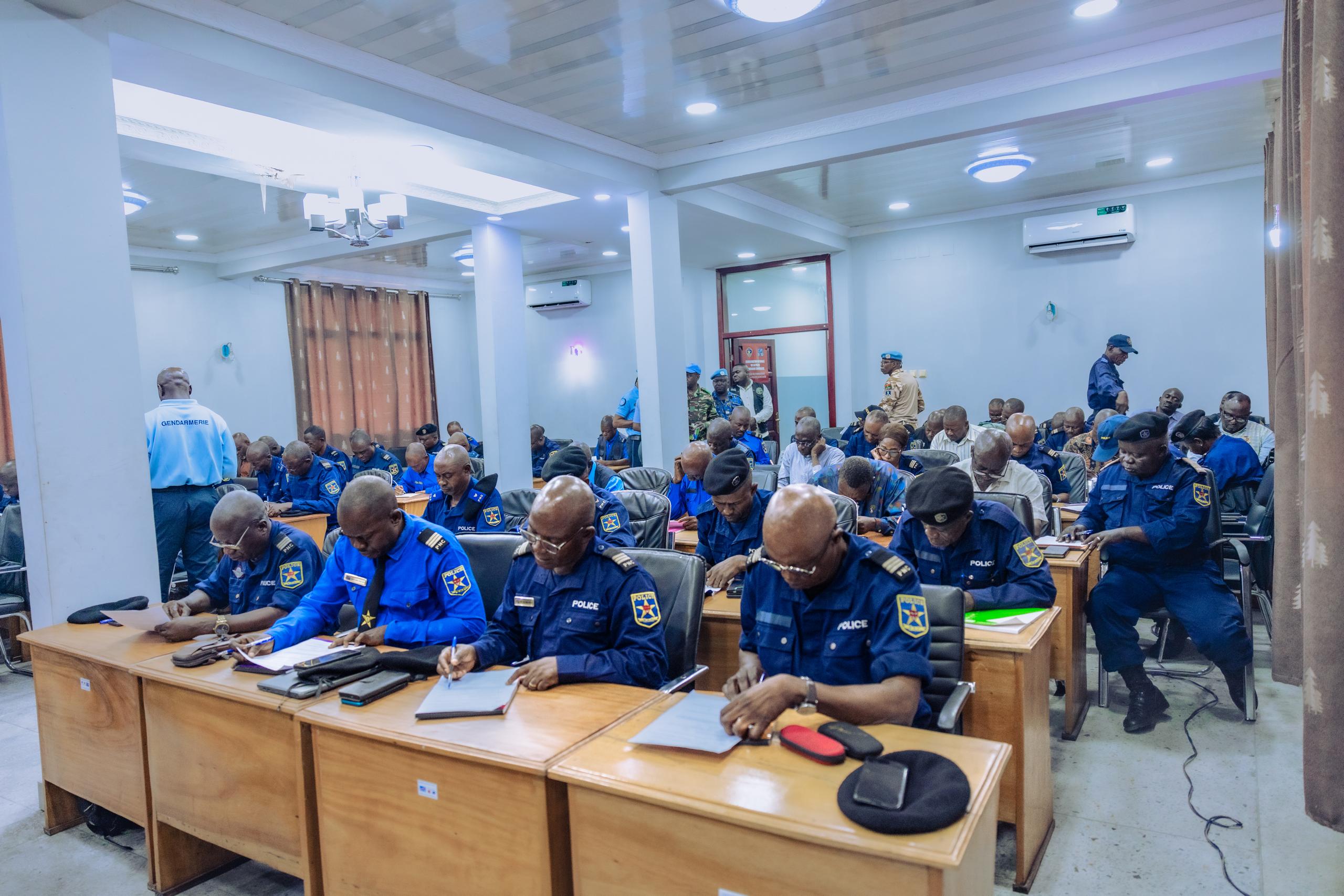 Photo: Group of people in blue uniforms seated at desks in a bright conference room.