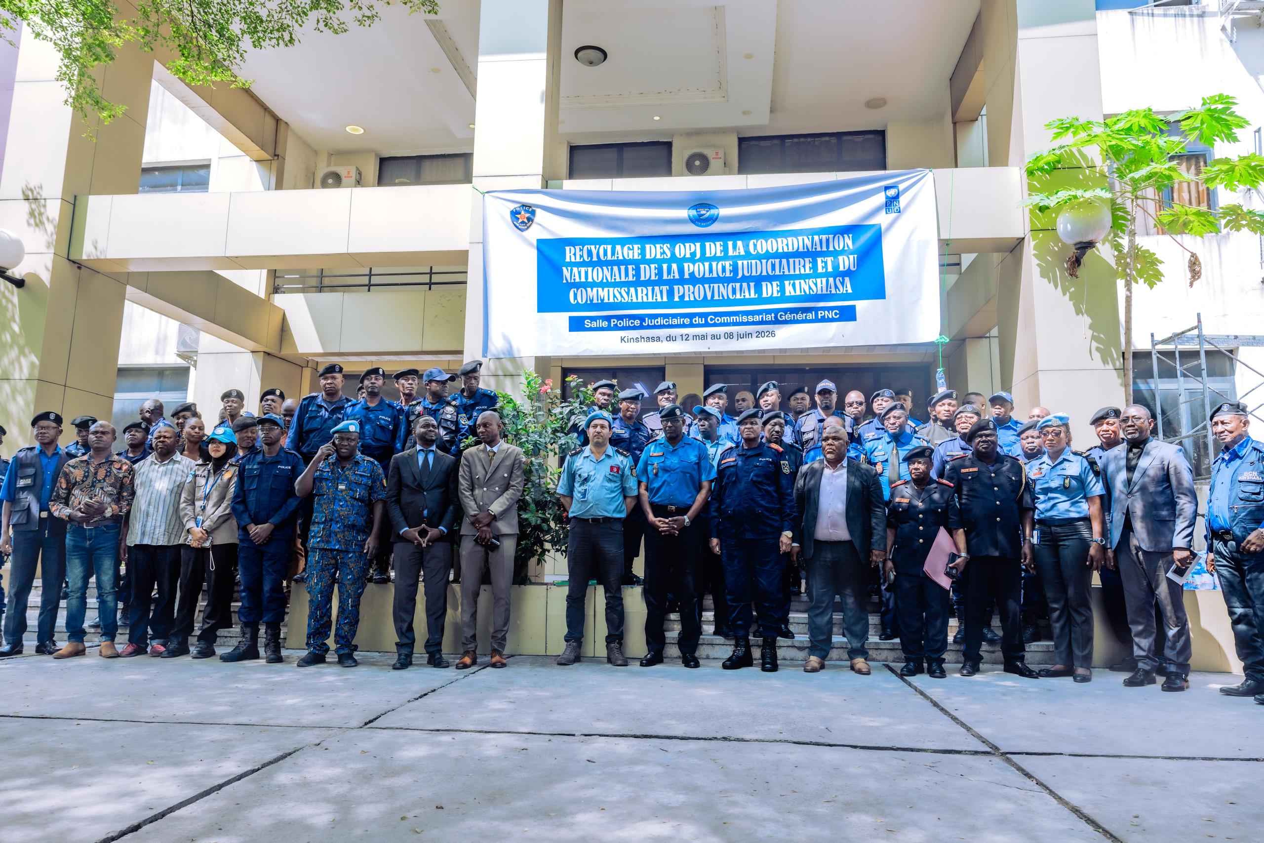 Outdoor group photo of people in blue uniforms in front of a building with a blue banner.