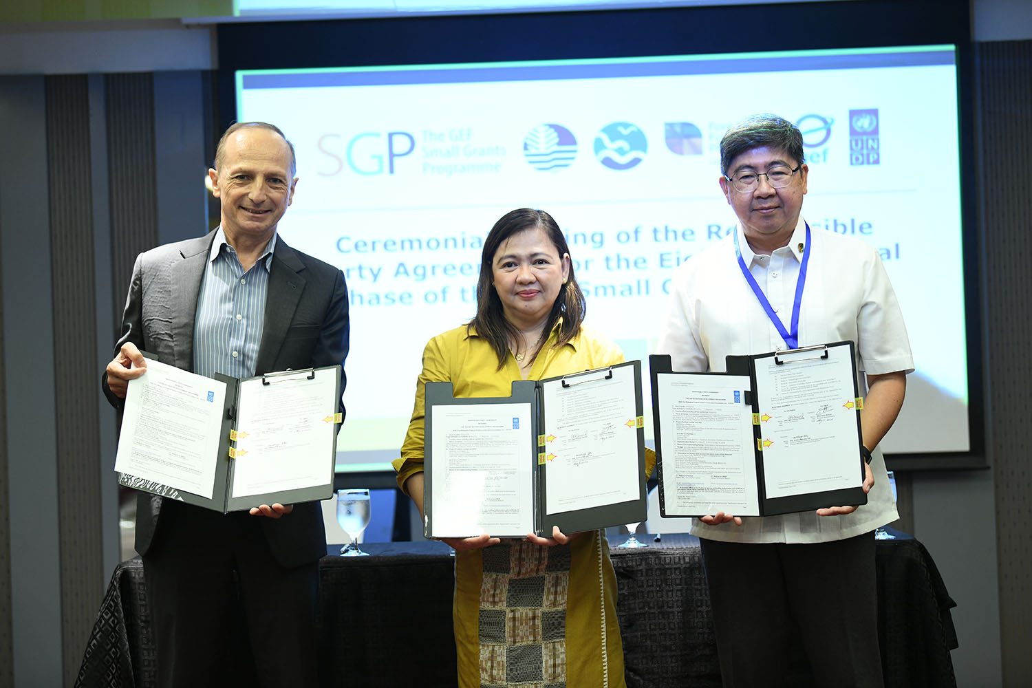 Three people on stage holding certificates at an award ceremony.