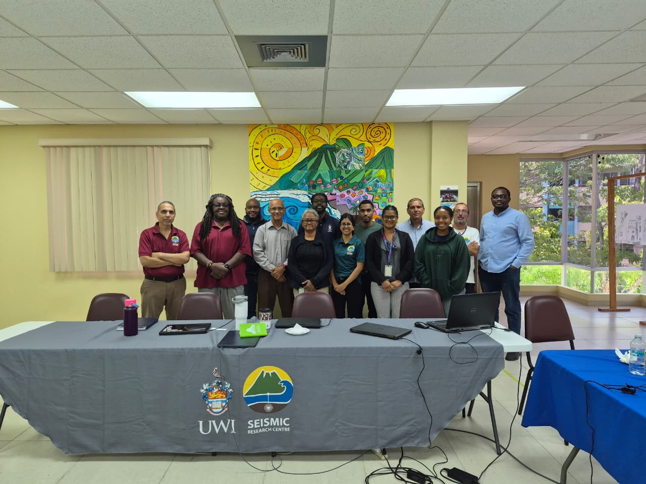 Group photo of students and staff standing behind a long table in a classroom with a colorful mural.