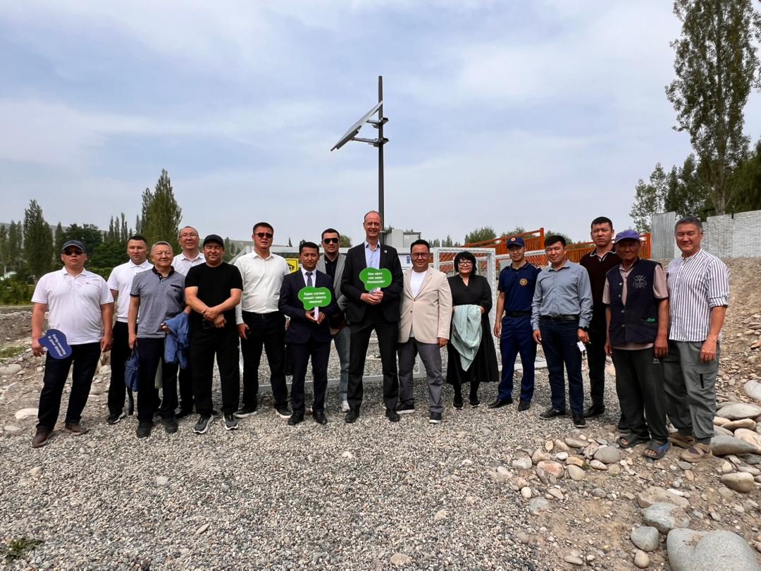 Group photo of people posing on a rocky site with a wind turbine tower in the background.