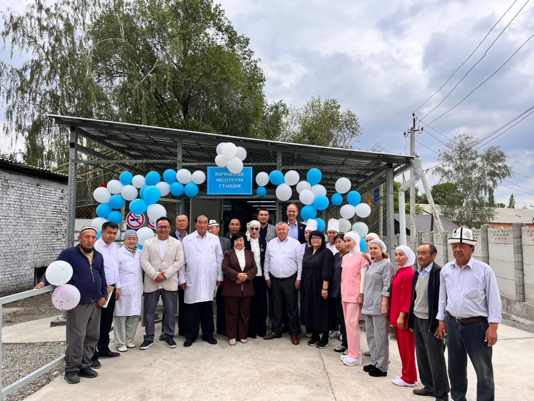 Group of people posing outdoors under a blue-and-white balloon arch in front of a building.