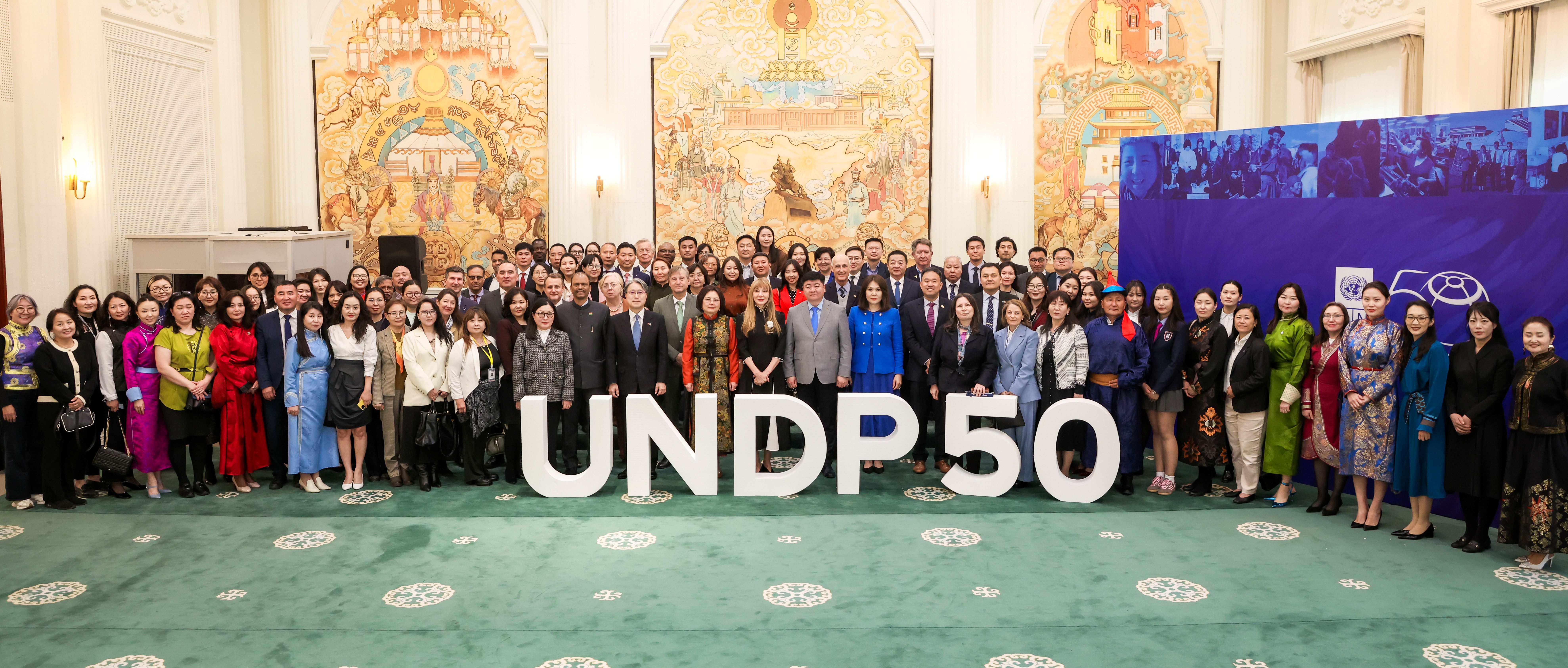 Photograph of a large diverse group posing in an ornate hall beside a UNDP 50 banner.