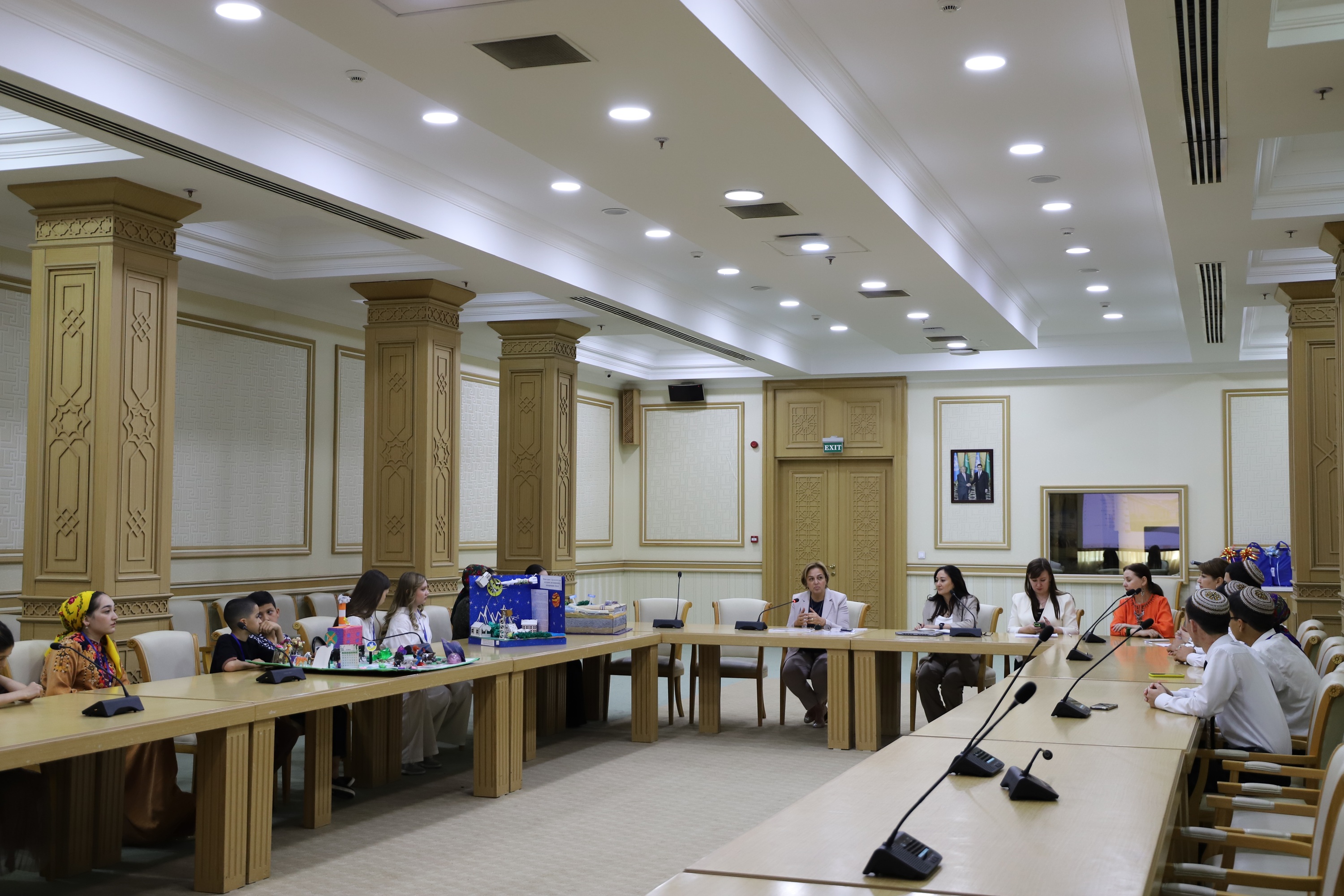 Photograph of a formal meeting in a bright conference room with people seated around a long table.