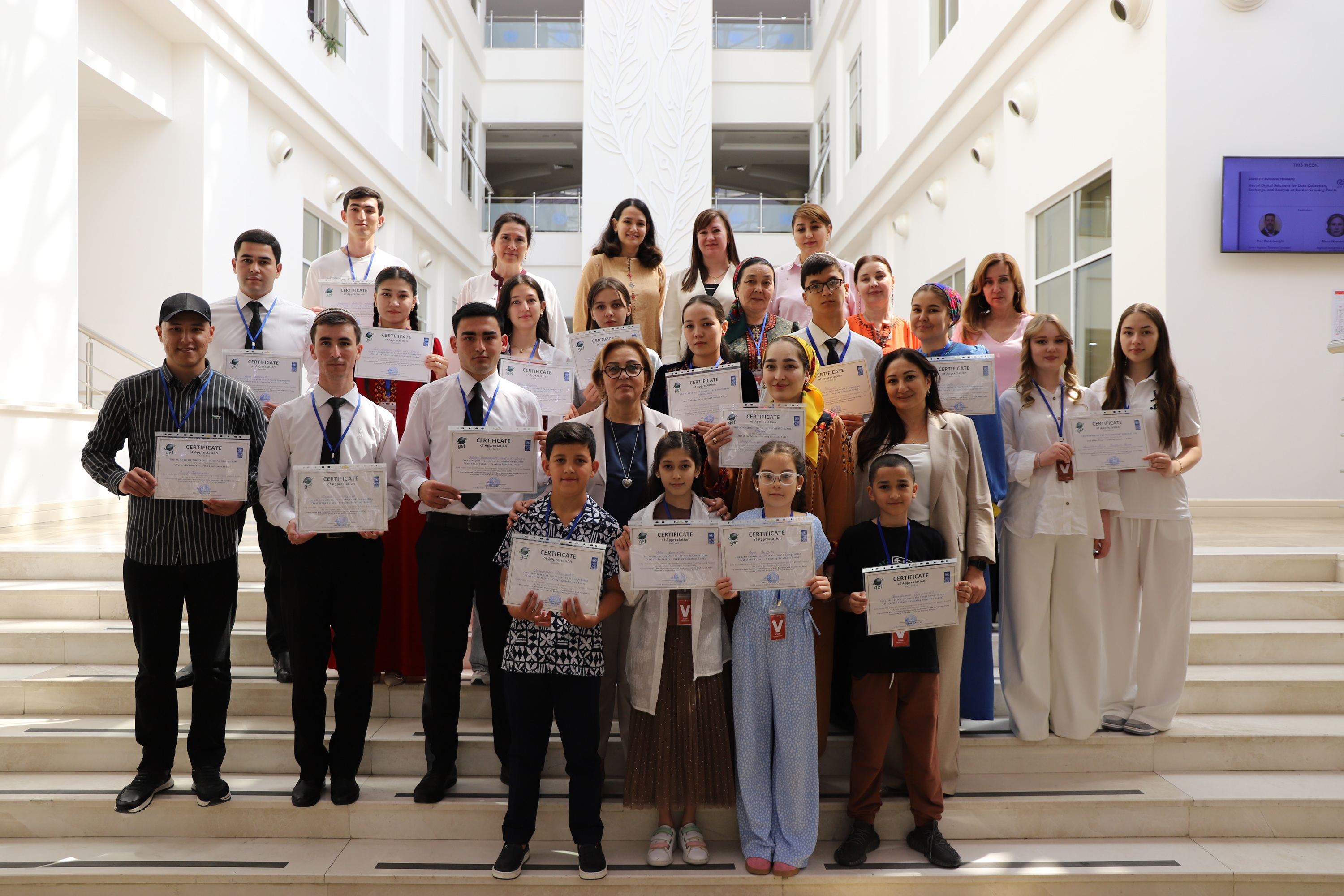 Photo of a large group of students and staff on a staircase, holding certificates.