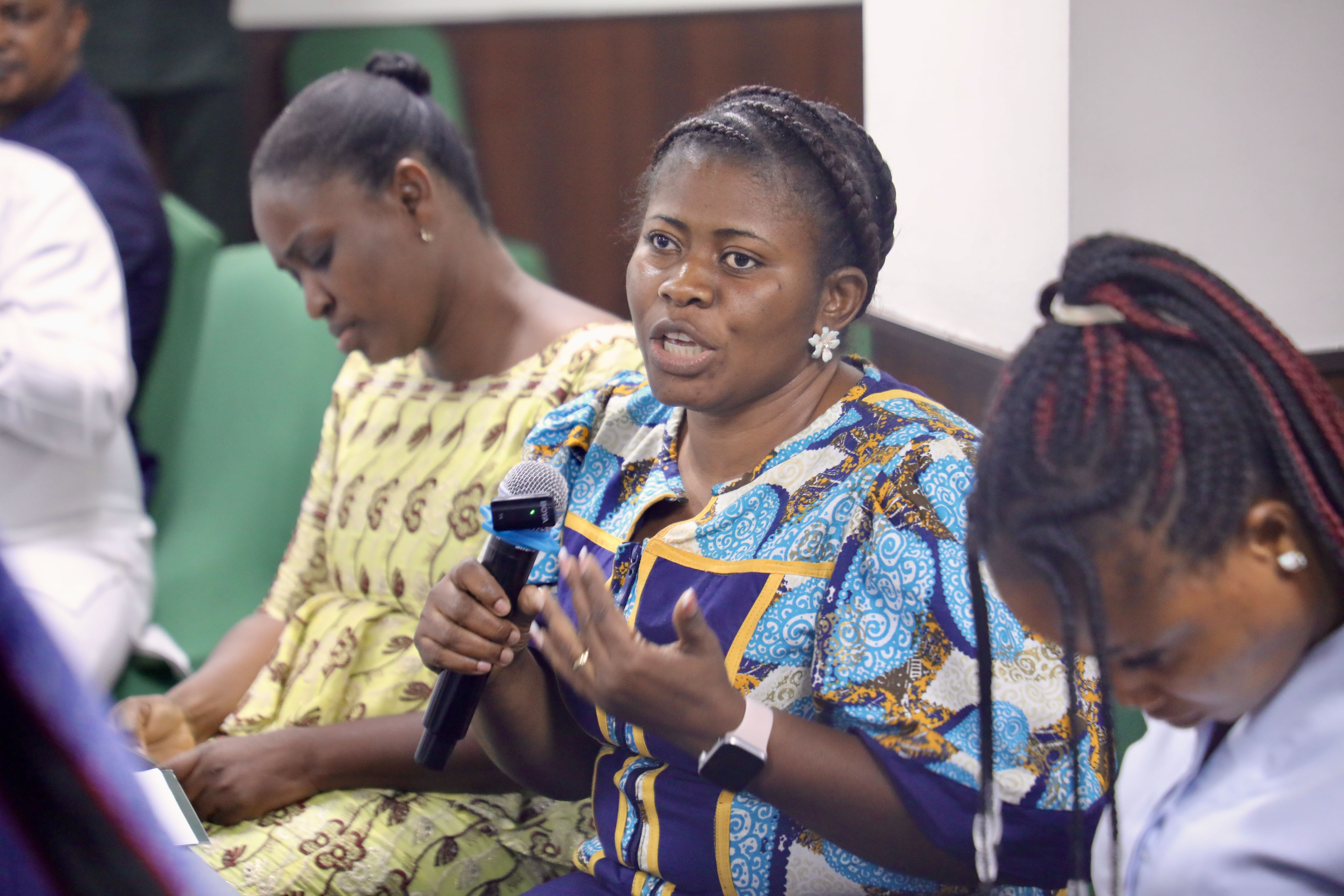 Woman in blue patterned dress speaks into a microphone at a group event.