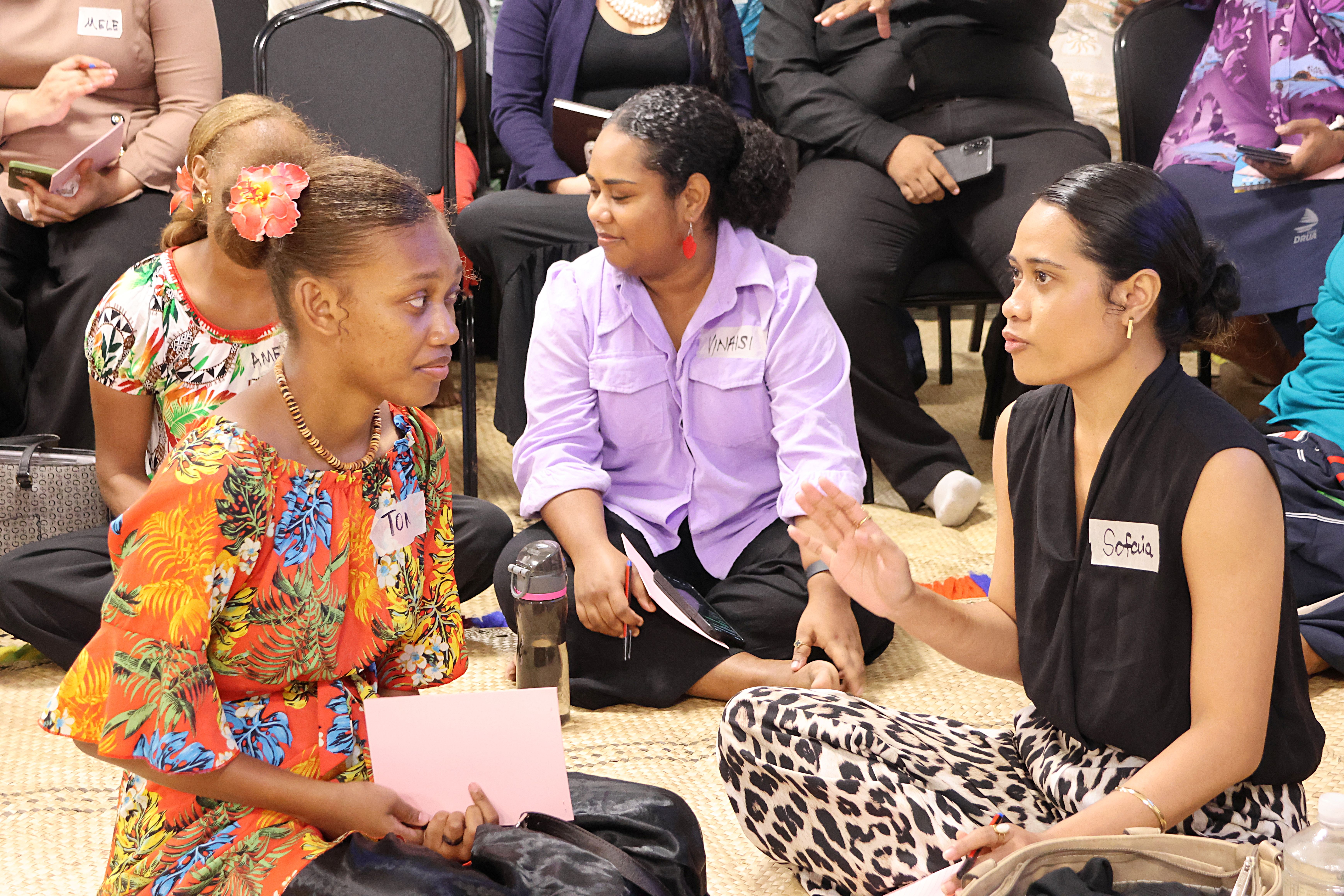 Group of people sitting on the floor in a circle, engaged in conversation; faces blurred.