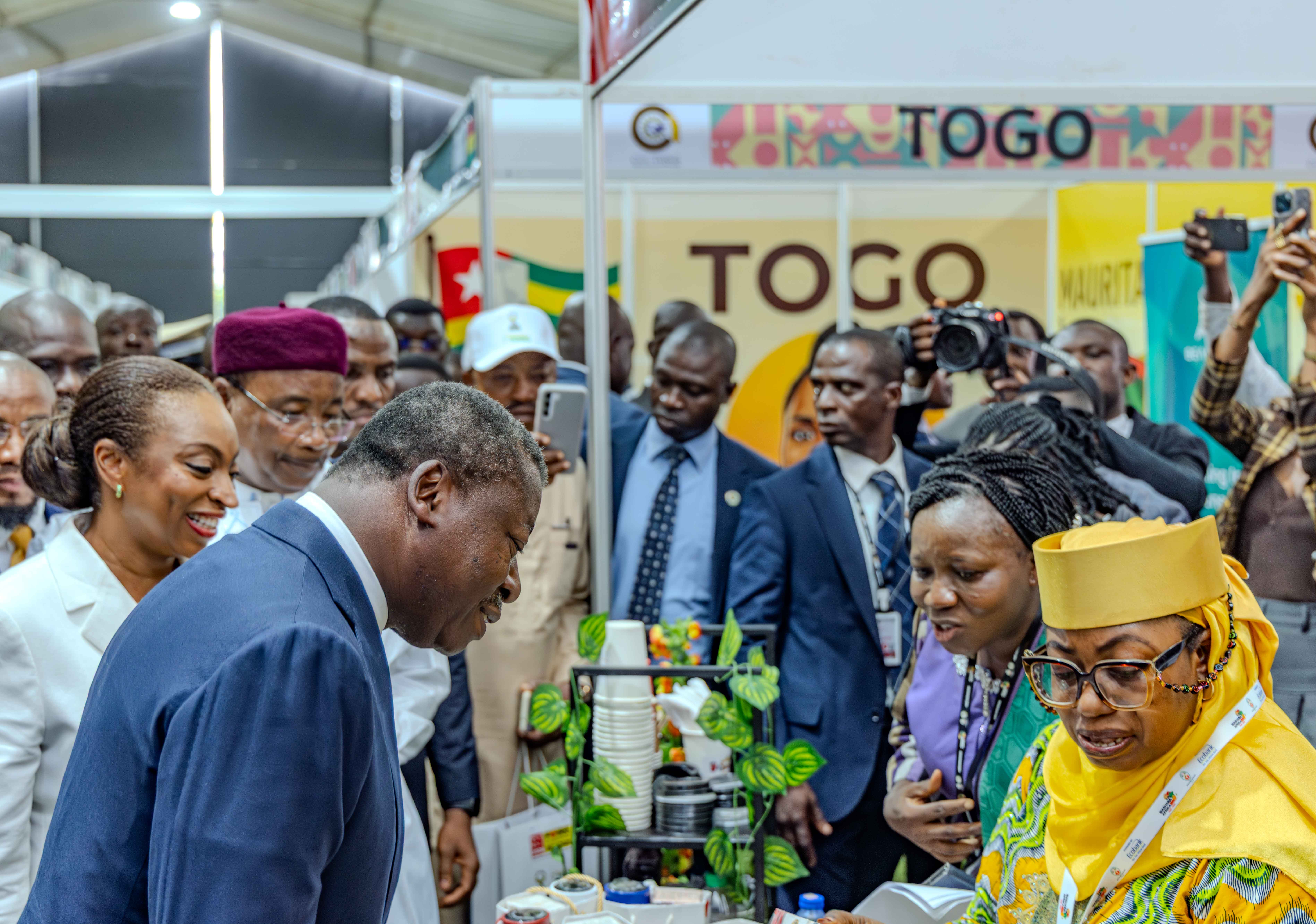 Crowded expo booth with TOGO signage; people in colorful attire examine a display.