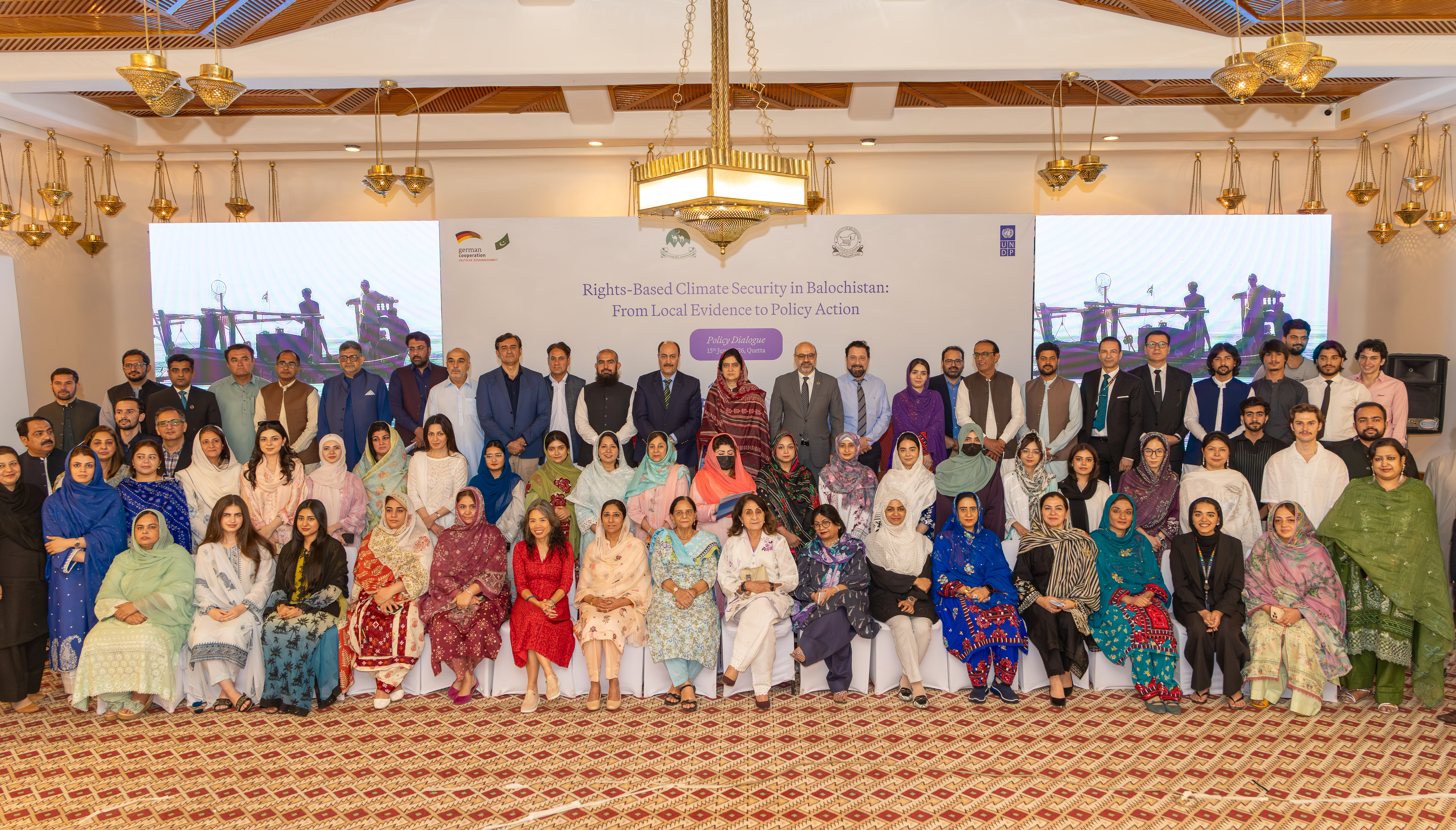 Large group of people in formal attire posing for a group photo in a banquet hall.