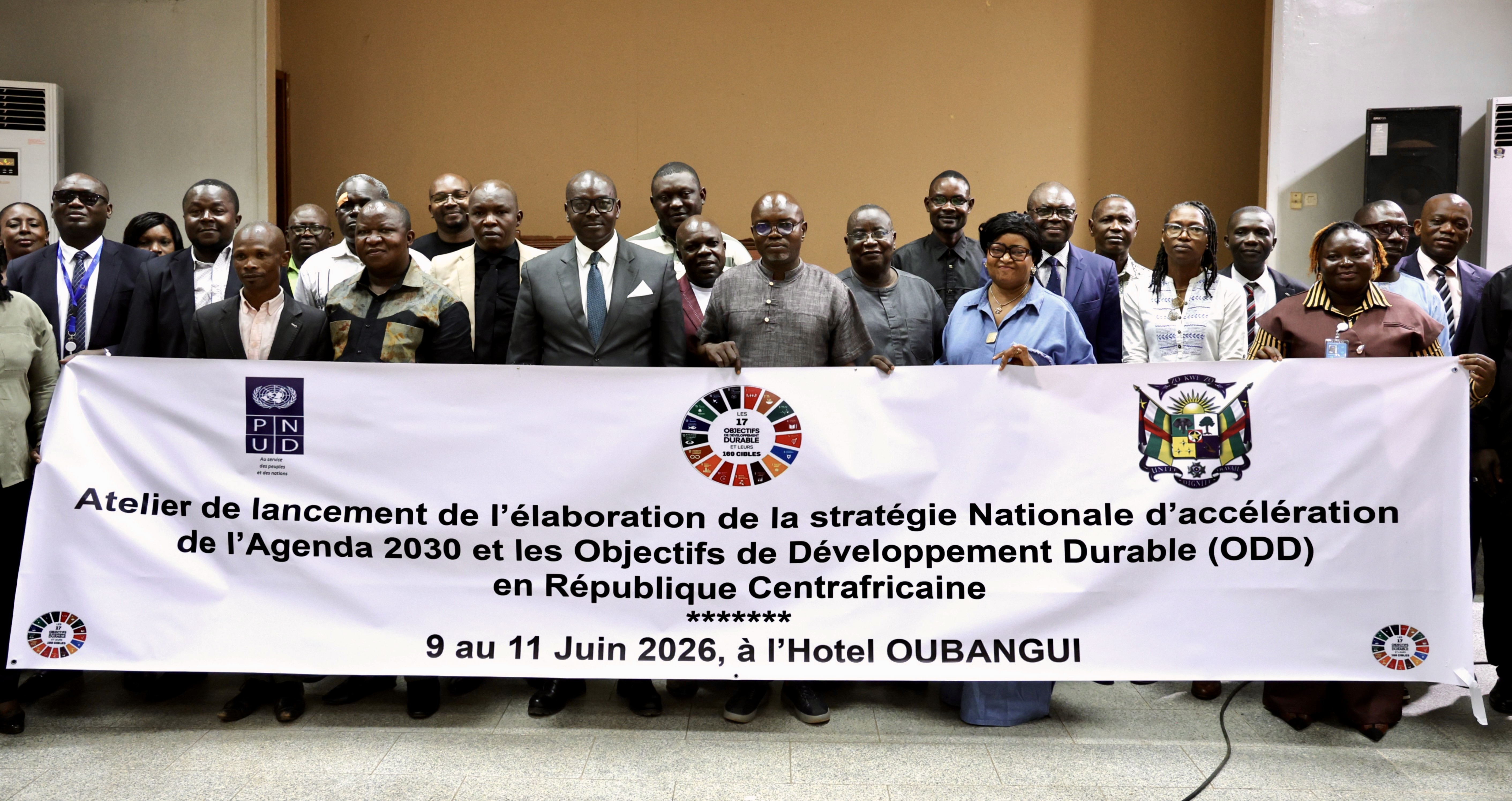 Group of officials in suits posing behind a long banner at a hotel conference.