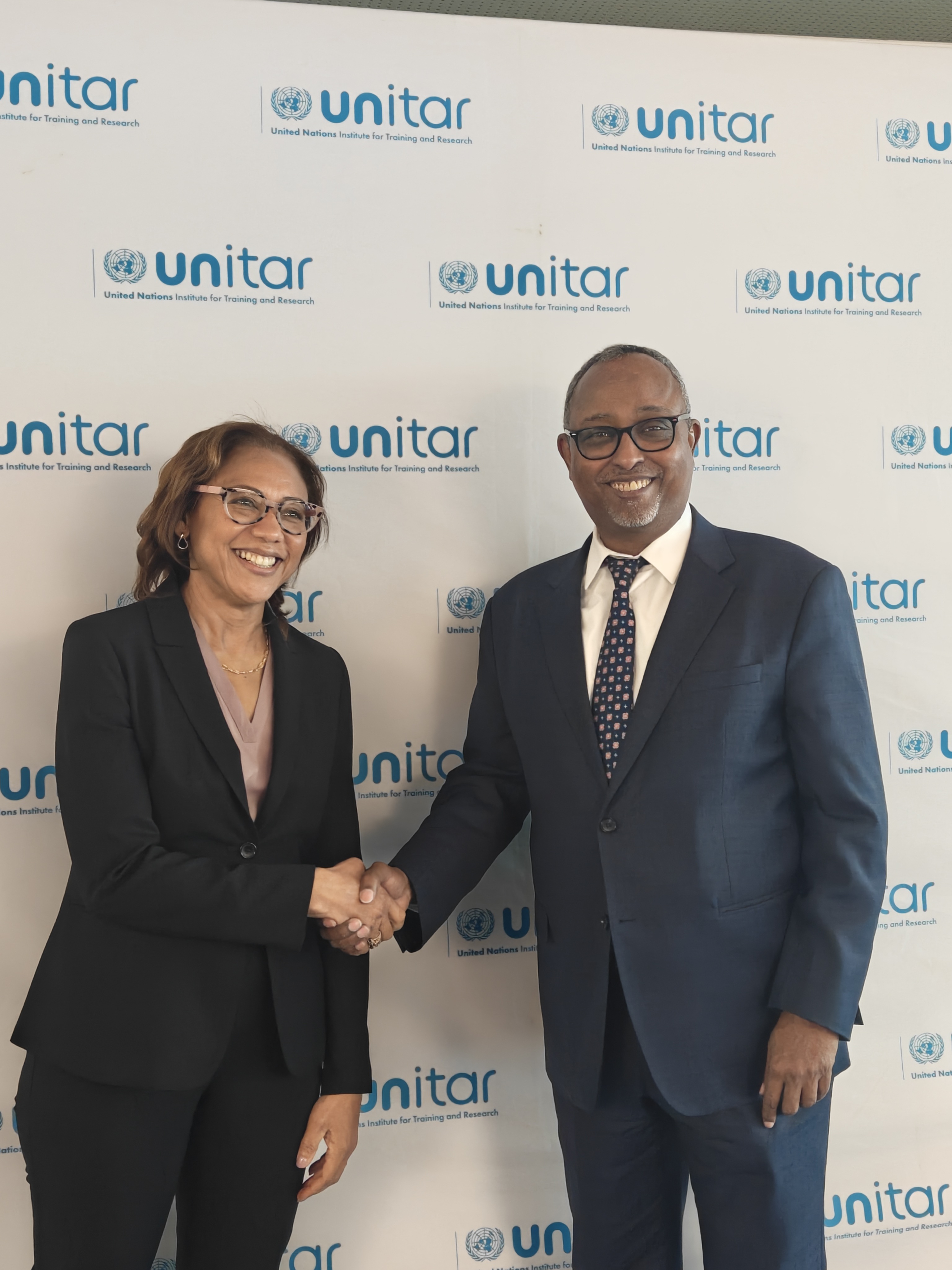 Photo: two professionals shake hands in front of a Unitar backdrop.