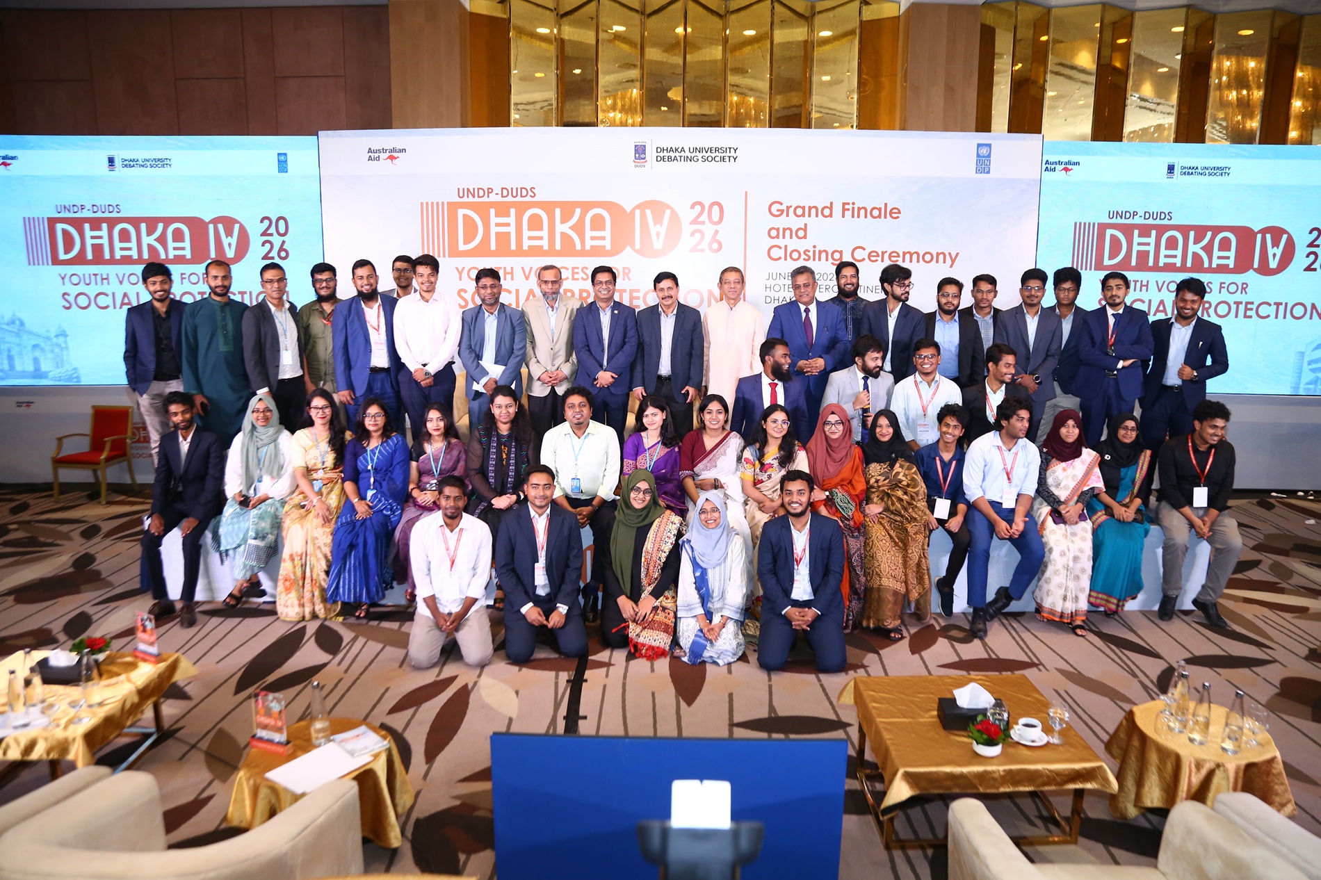 Group photo of conference attendees in formal wear, standing on a stage with banners behind.