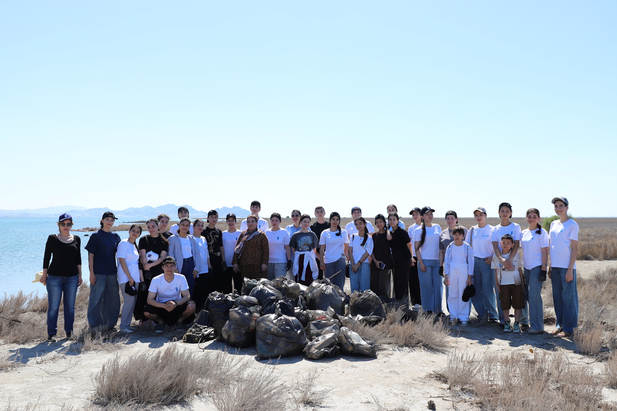 Group of volunteers outdoors in an arid desert landscape, standing behind piles of trash bags.