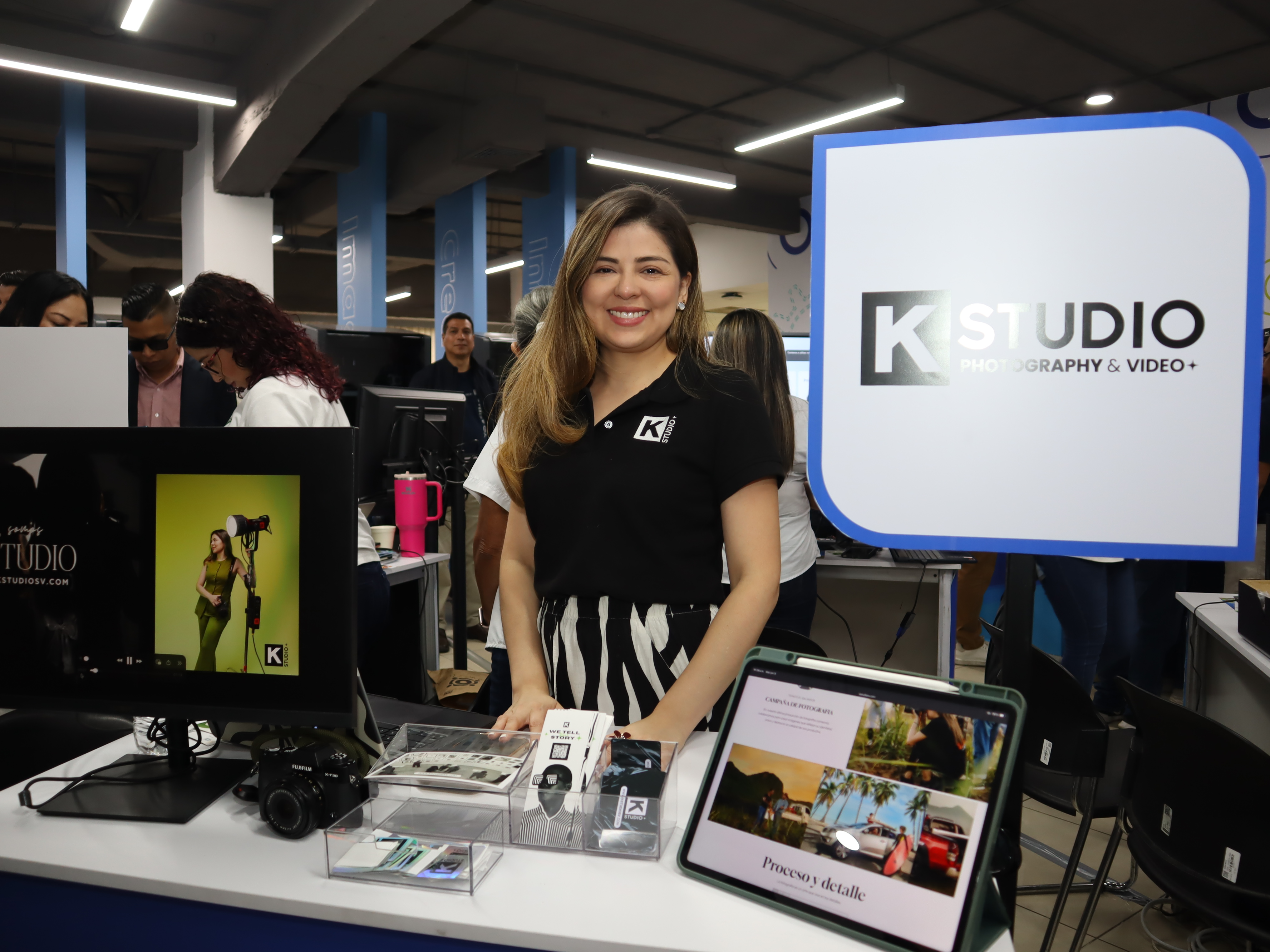 Smiling woman in black at a tech expo booth with laptops and a K Studio sign.
