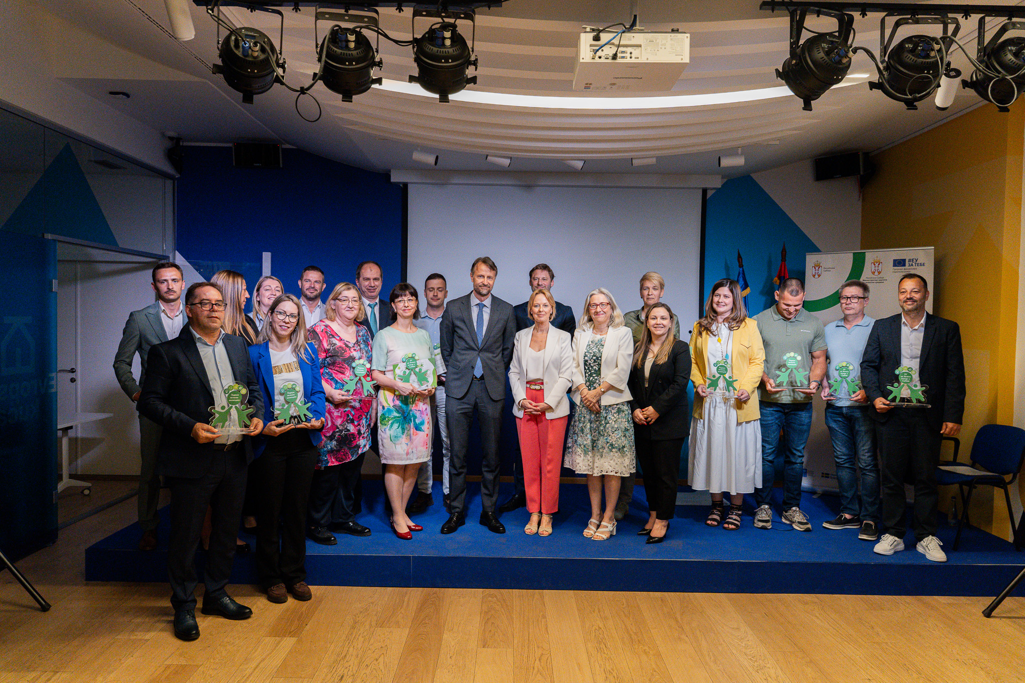 Group of diverse people posing on a stage with blue and yellow backdrop.