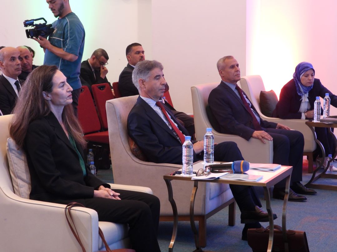 Photograph of men and women in suits seated on a panel at a conference.
