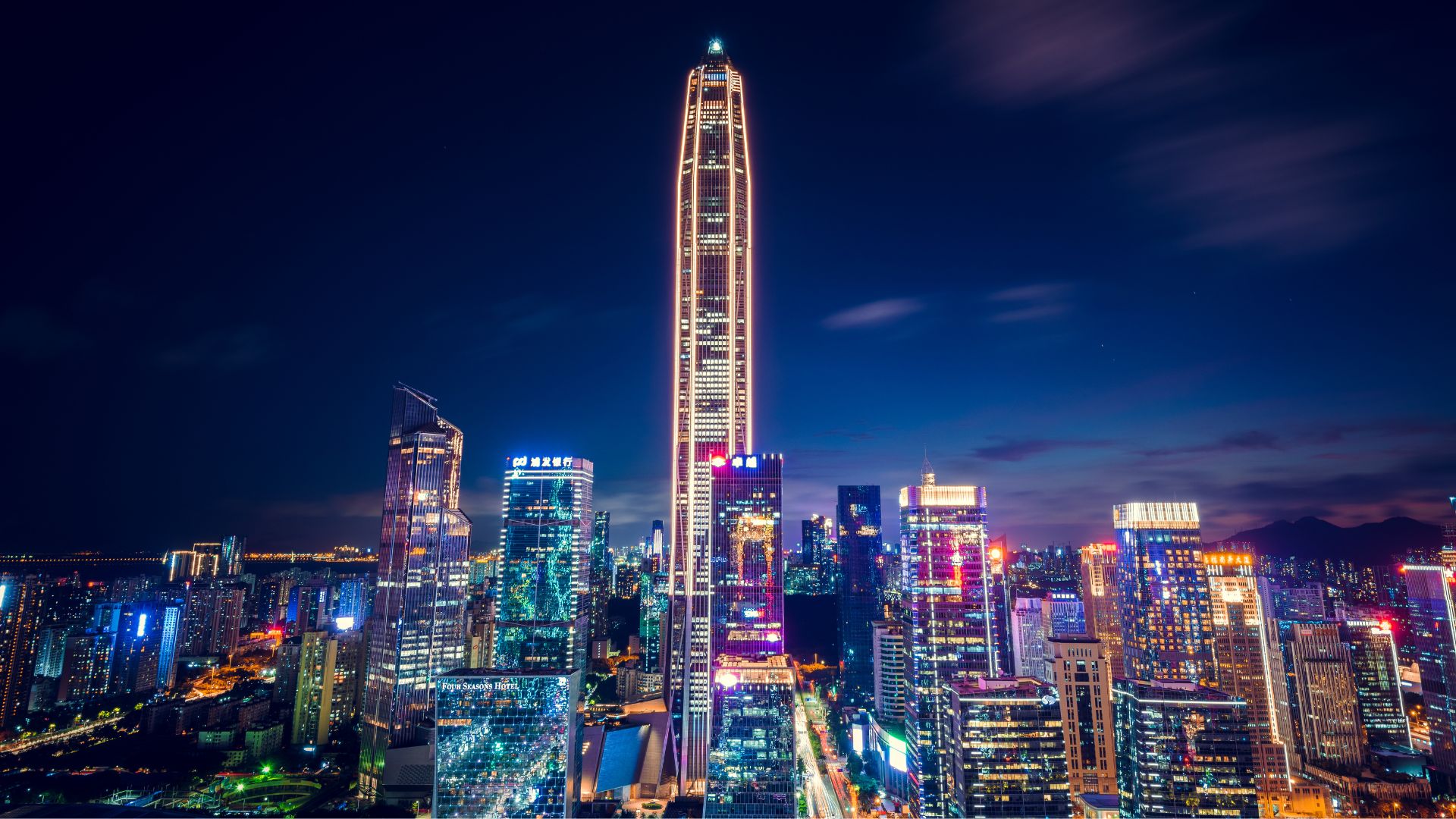 Nighttime city skyline with neon-lit skyscrapers and a tall central tower.