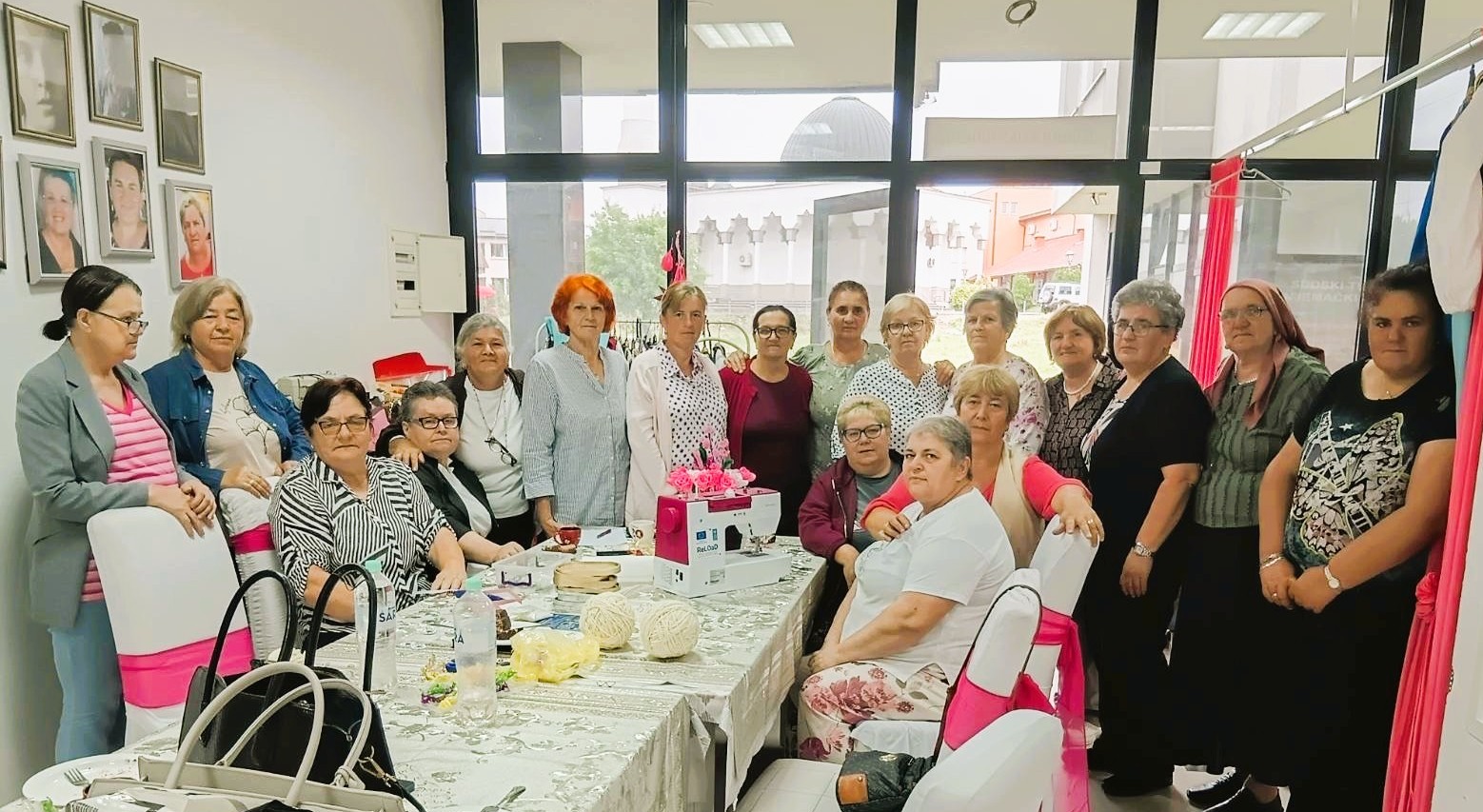 Group of people gathered around a long table with food in a bright room.