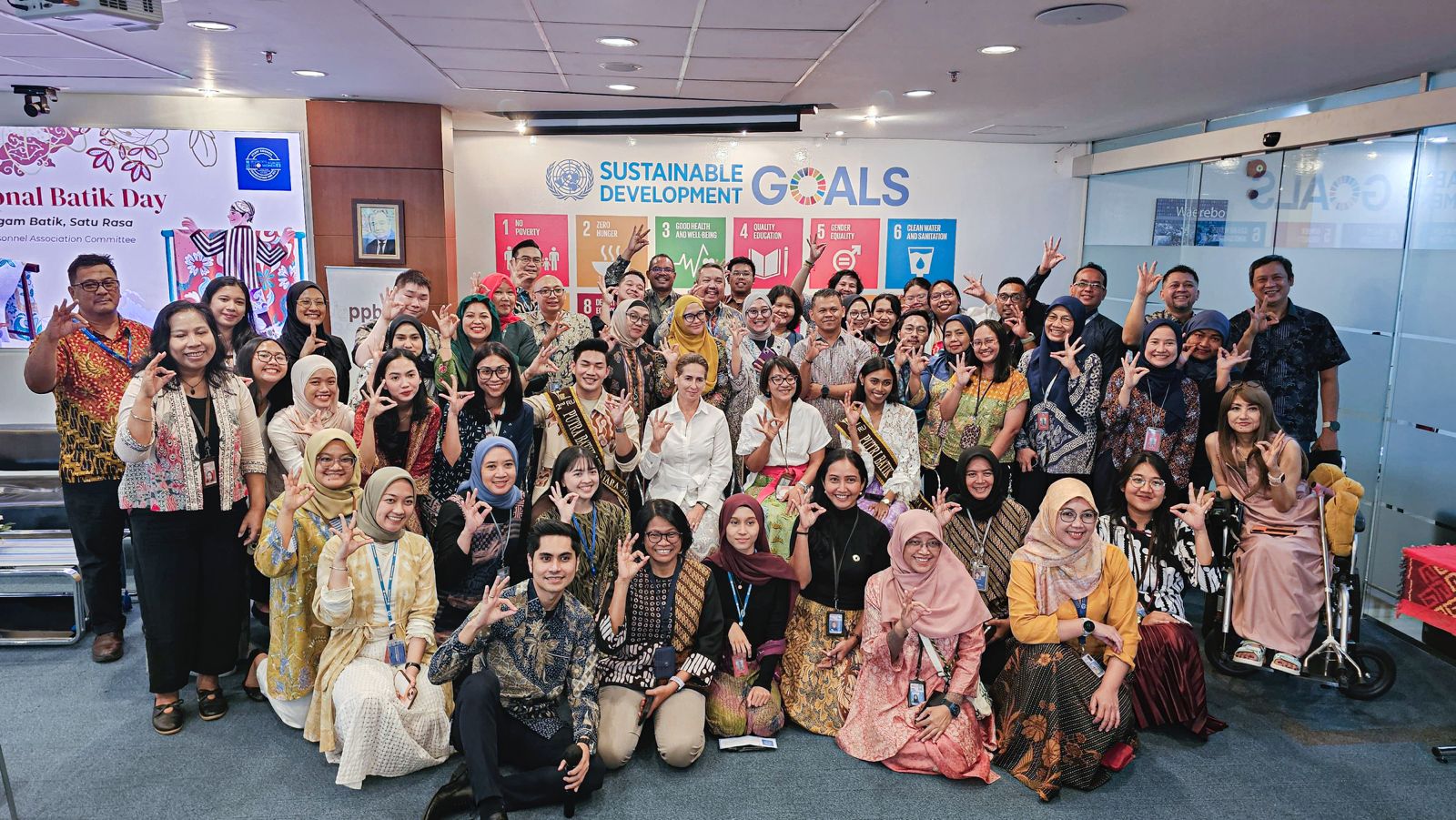 Group photo of diverse people in colorful outfits in a conference room with GOALS banners.