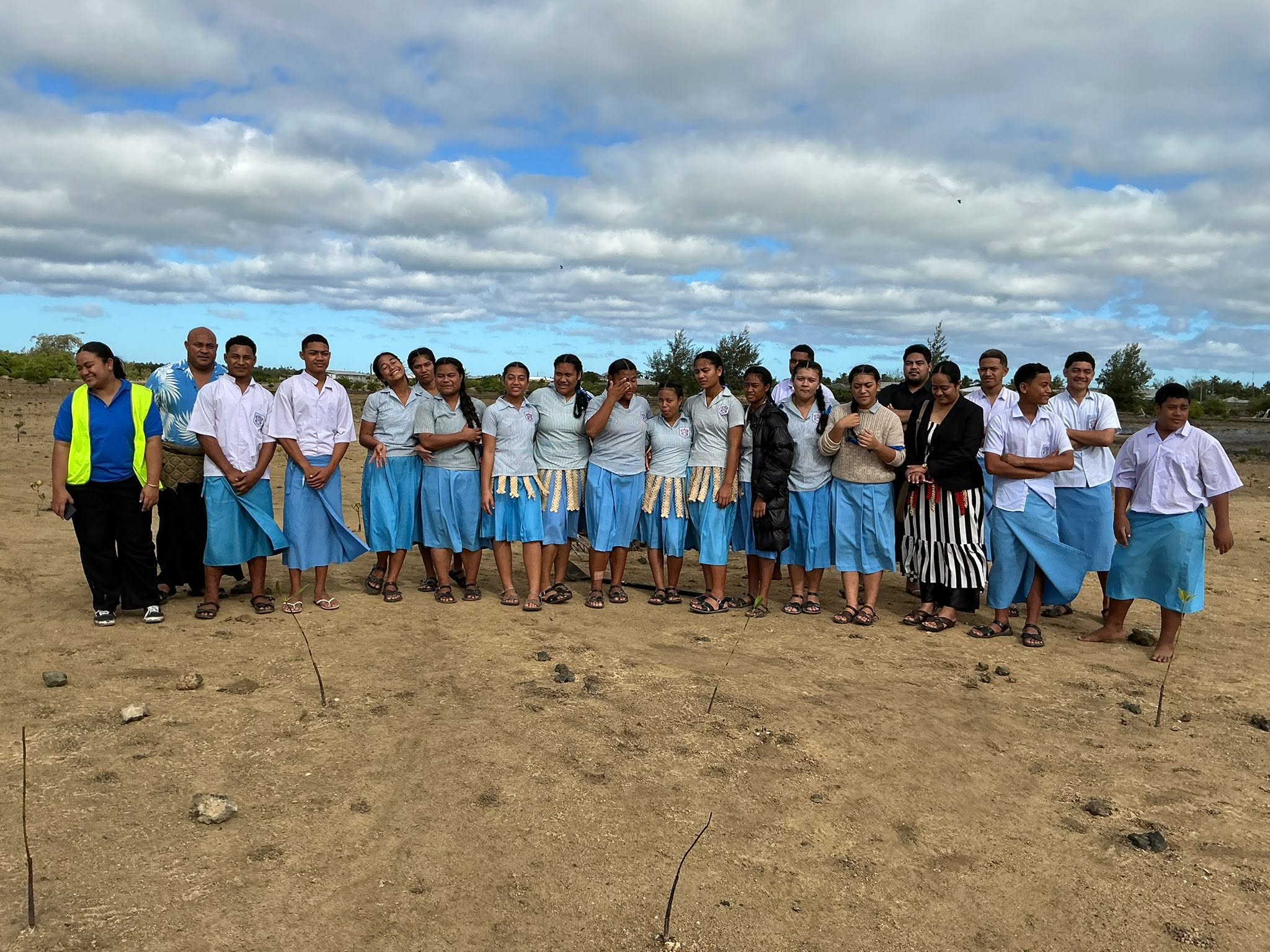 Group of people posing on a sandy beach with the ocean and blue sky behind.