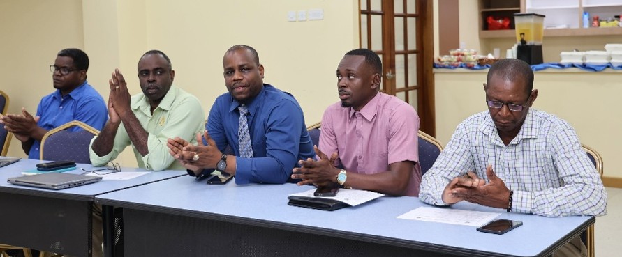 Five men seated at a long table in a meeting room with papers and a microphone.