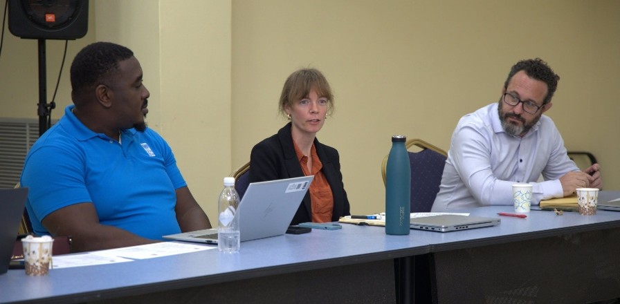 Three panelists sit at a table with papers and a laptop.