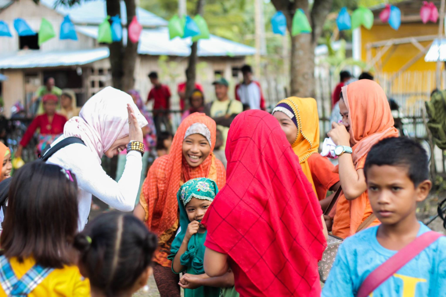 Group of women and children in colorful outfits at an outdoor market with tents and bunting.