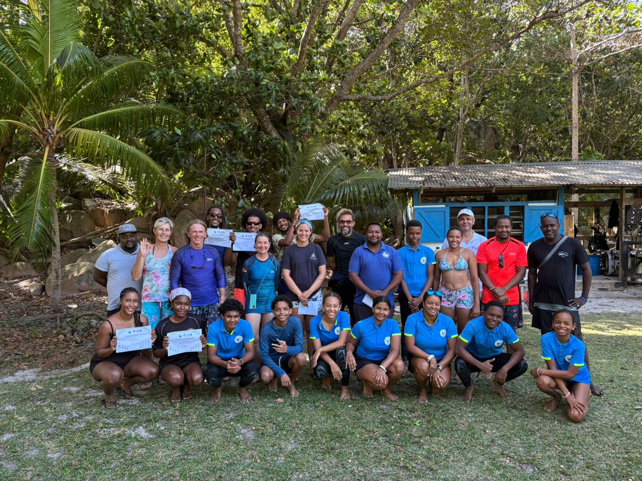 Group of people in blue shirts posing outdoors in a tropical palm-filled setting.