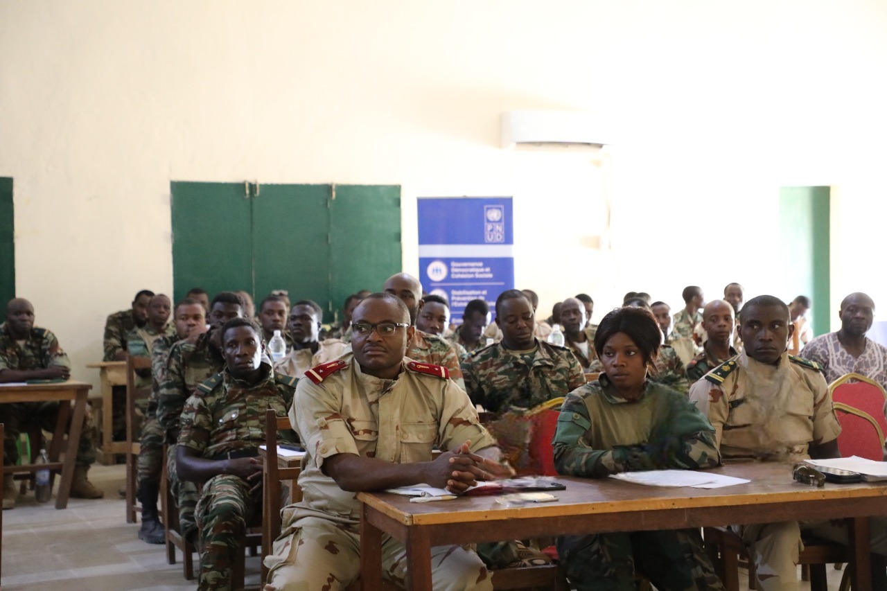 Group of uniformed officers and civilians seated in a classroom during a meeting.